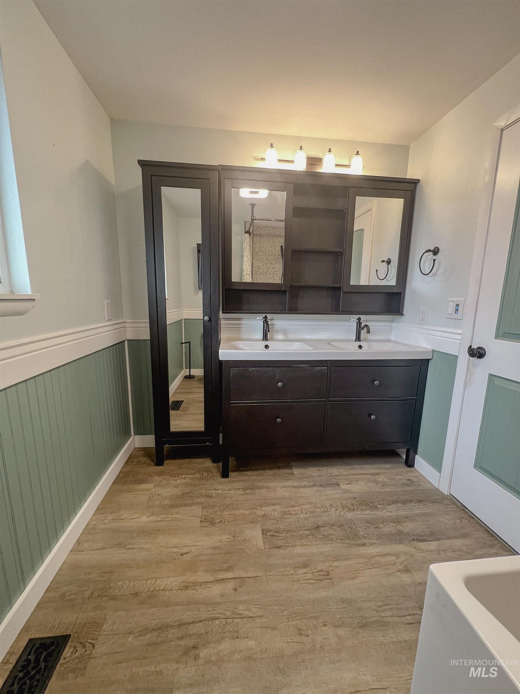 Bathroom featuring a wainscoted wall, double vanity, and light wood-style floors