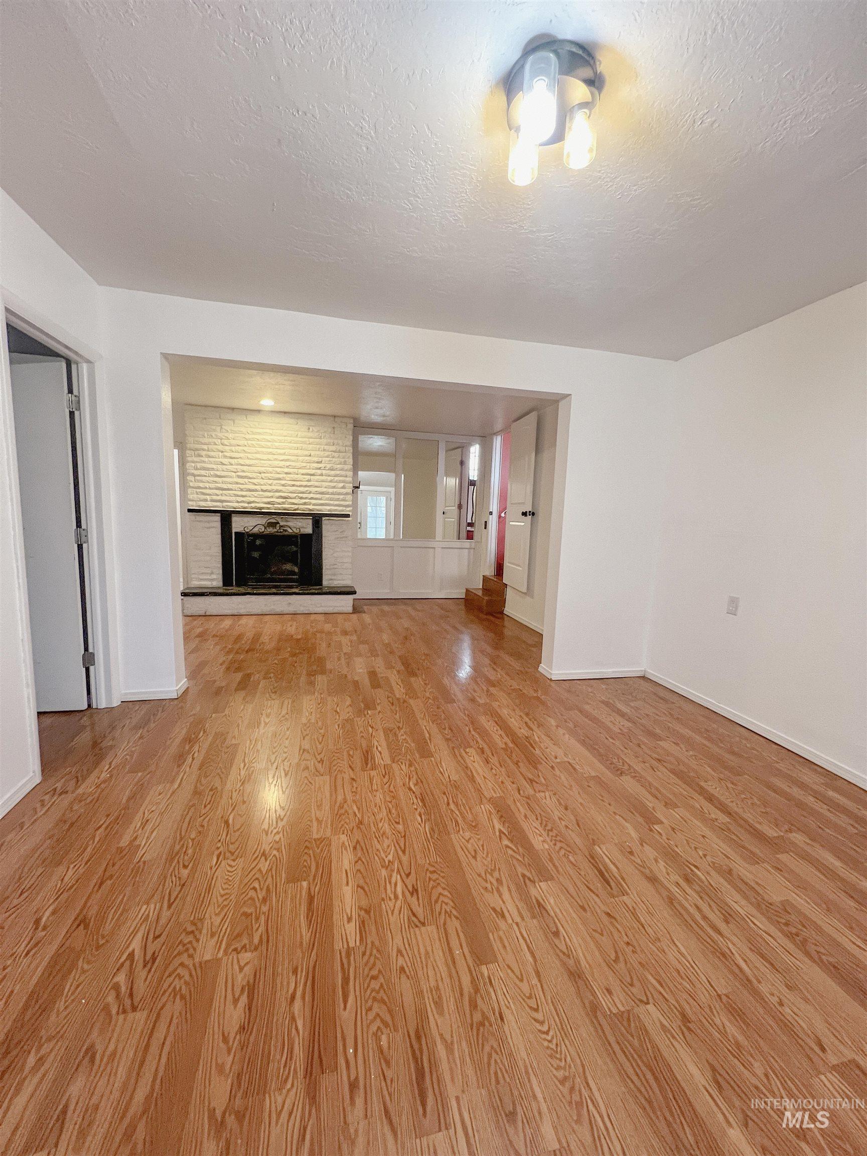 Unfurnished living room with light wood finished floors, a fireplace, and a textured ceiling