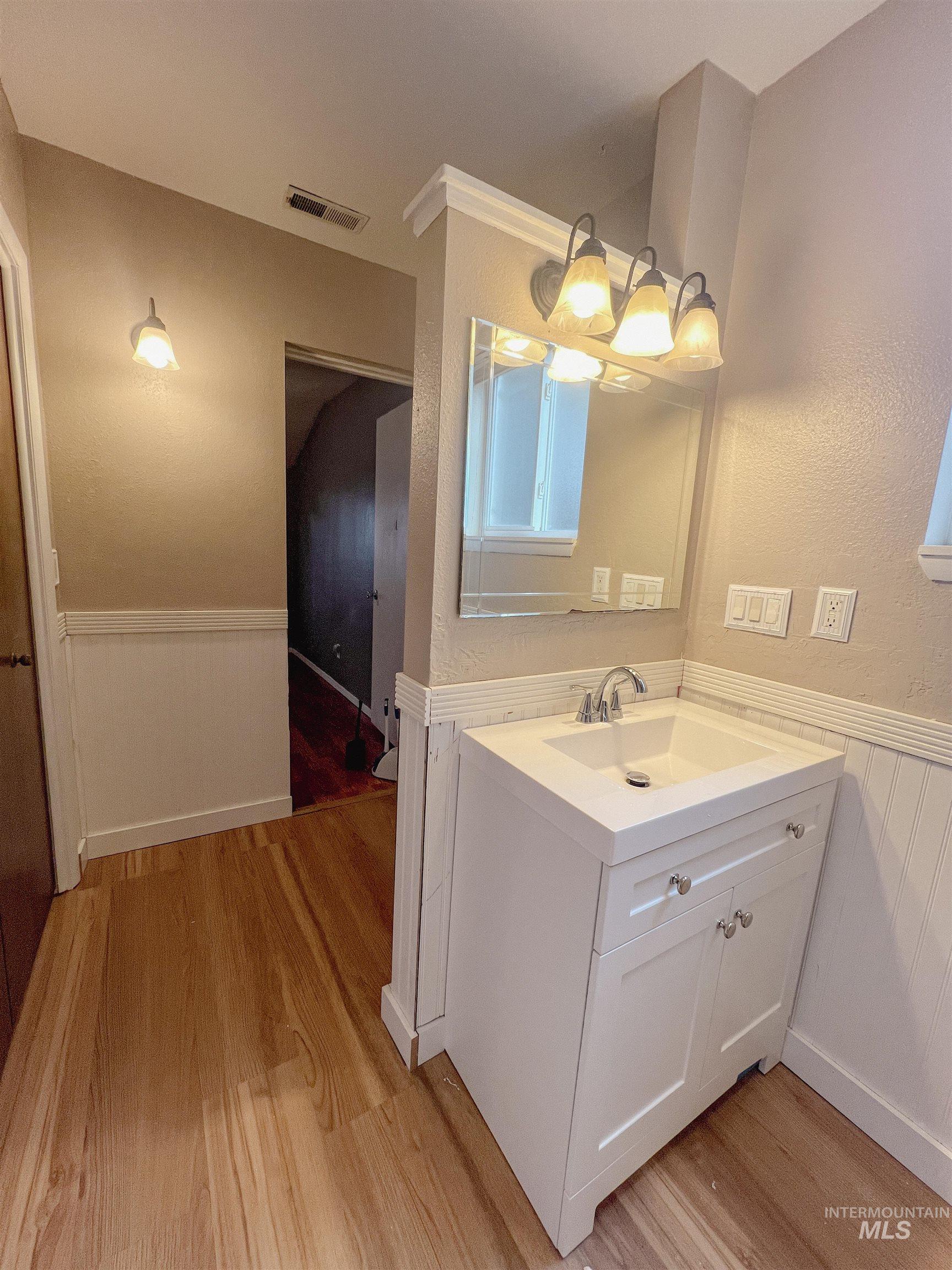 Bathroom featuring a wainscoted wall, vanity, light wood-type flooring, and a textured wall