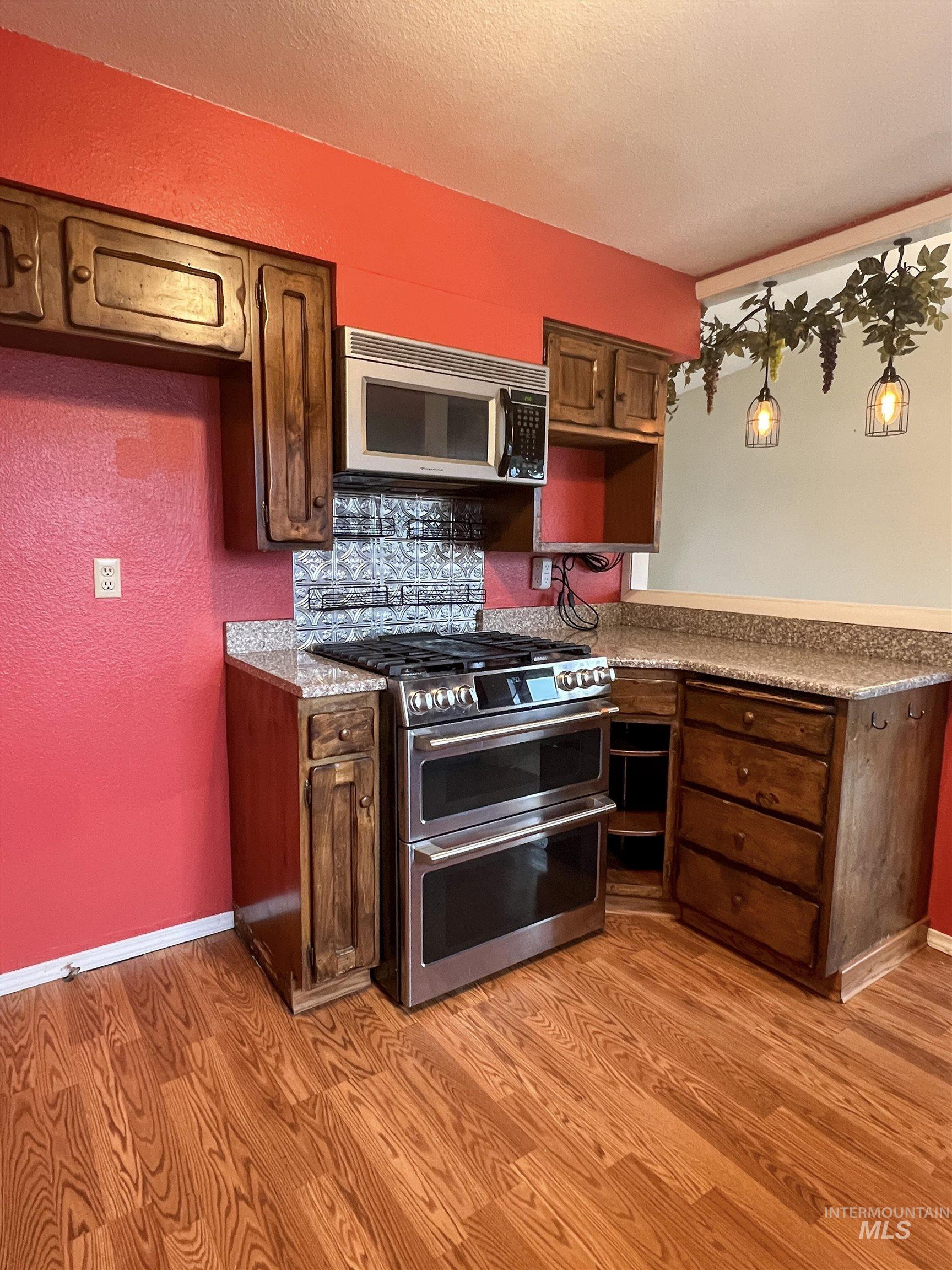 Kitchen with stainless steel appliances, light countertops, light wood-type flooring, dark wood finish cabinetry, and a textured ceiling