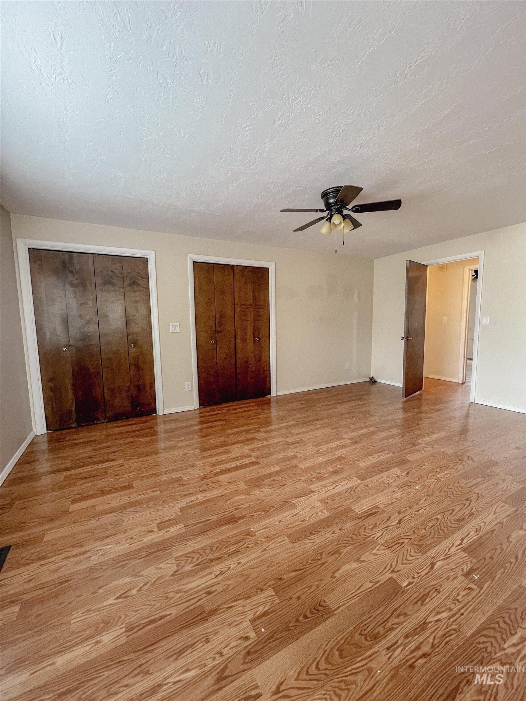 Unfurnished bedroom featuring two closets, light wood finished floors, ceiling fan, and a textured ceiling