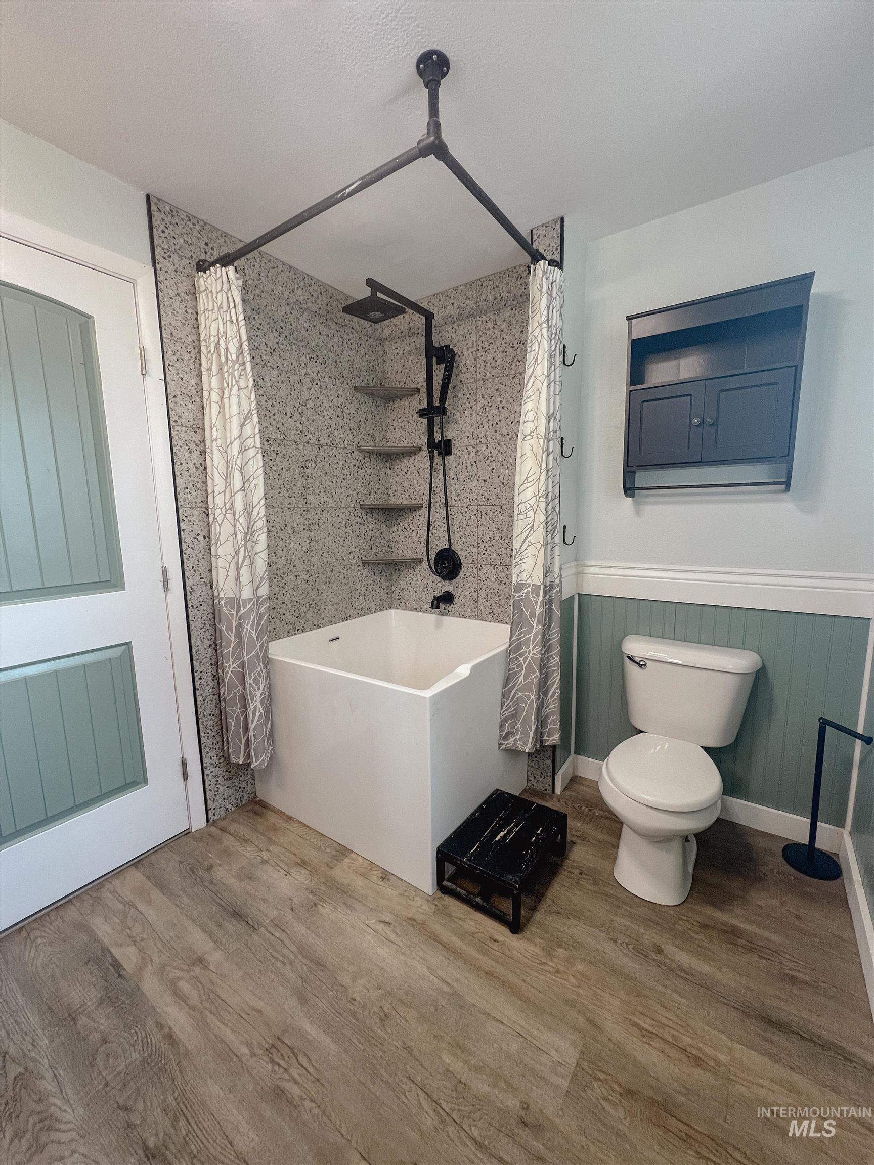 Full bath with wainscoting and wood finished floors