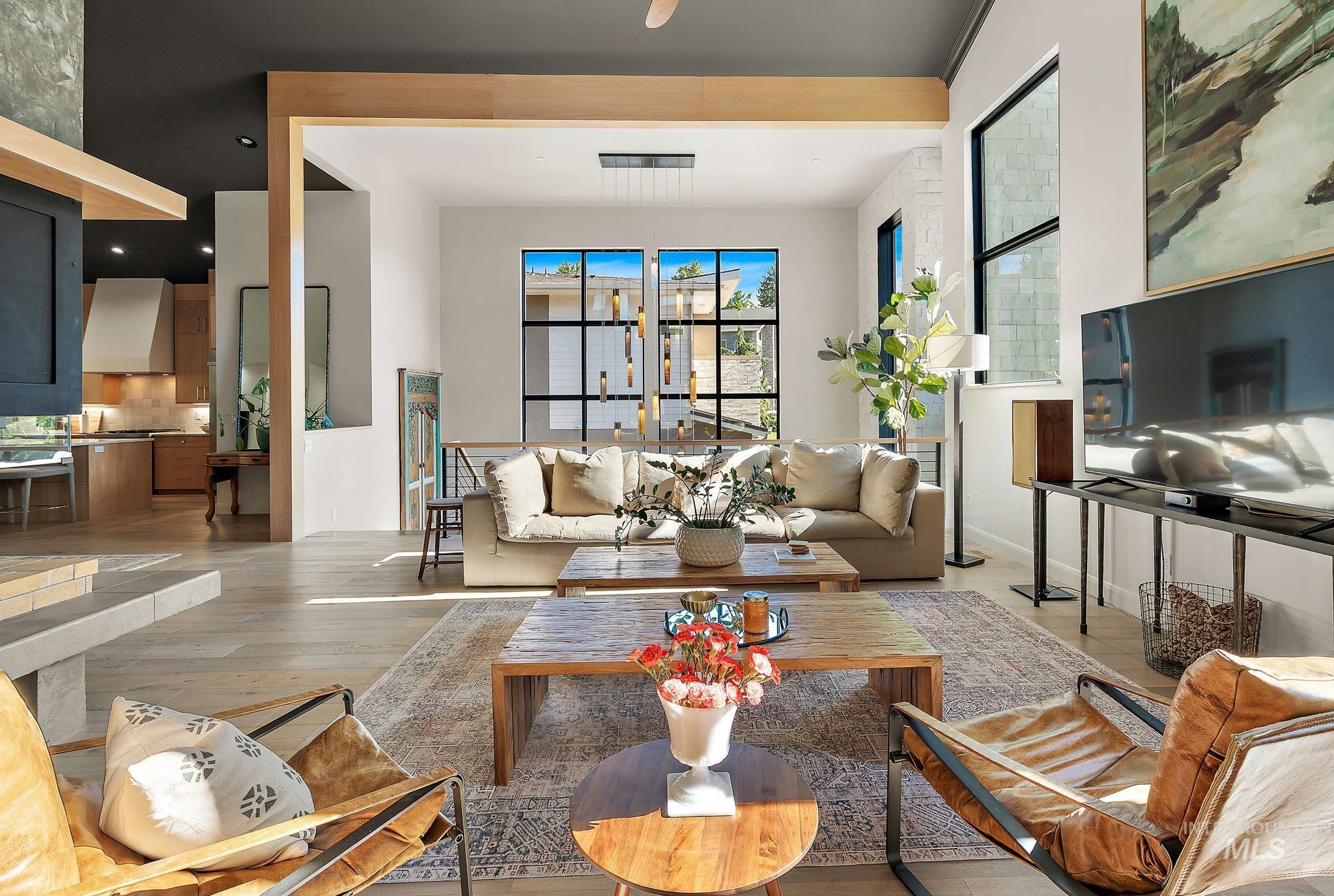 Spacious living area featuring light wood-finish flooring, a contemporary fireplace with a stone hearth, and extensive natural light from multiple large windows