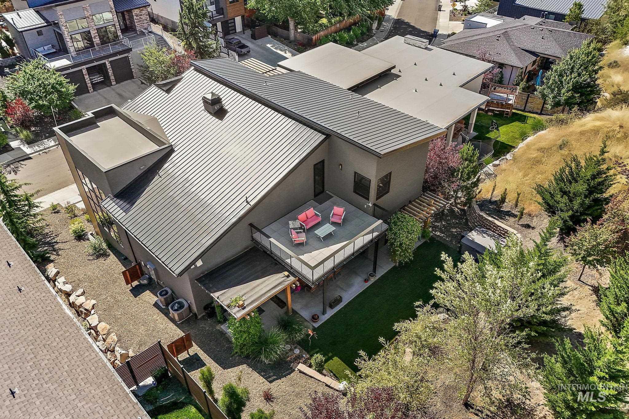 Contemporary residence featuring a dark metal roof, a second-story outdoor deck, and established landscaping