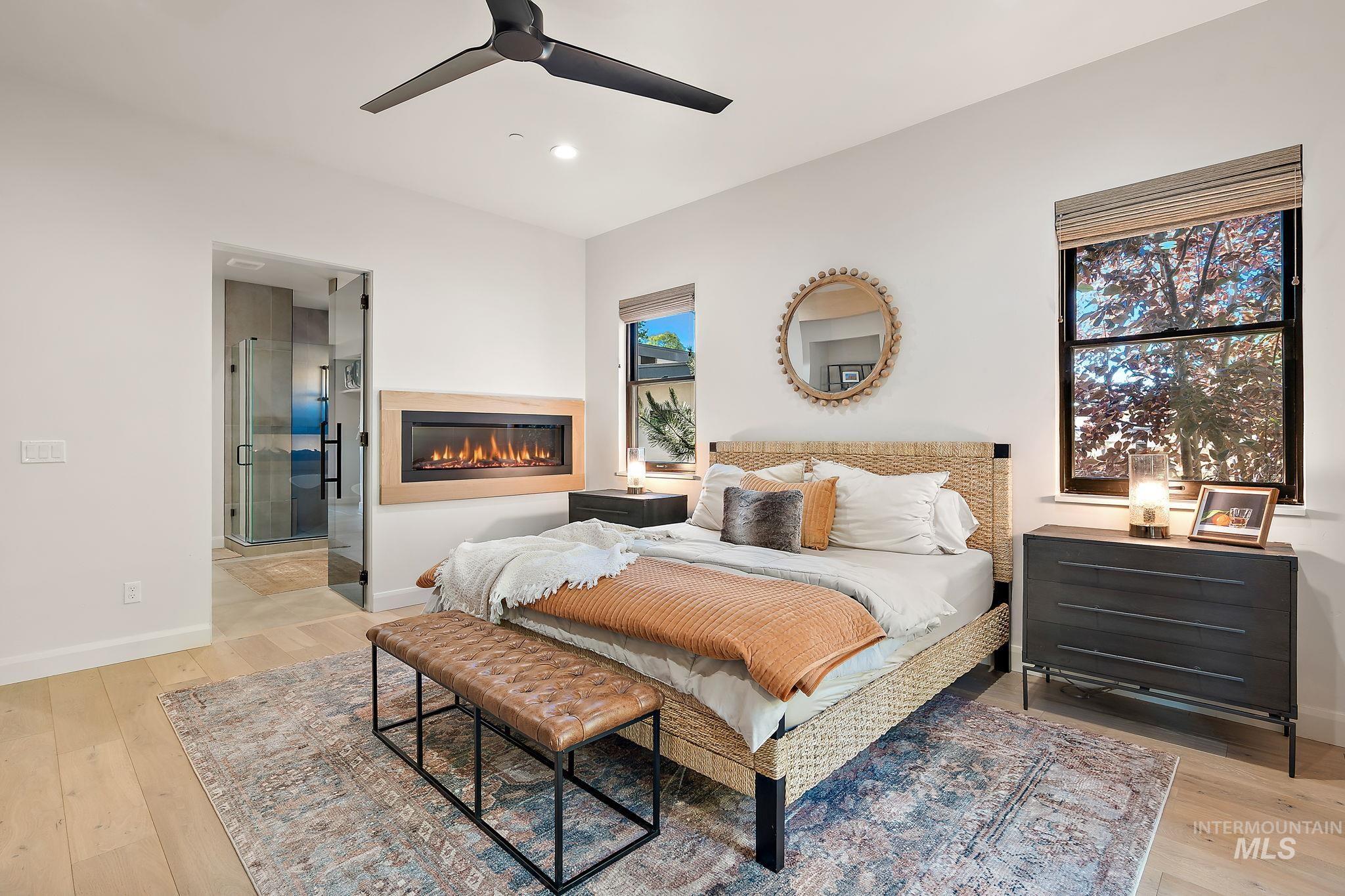 Spacious room featuring a wall-mounted linear fireplace with a light wood surround, two windows with blinds, a ceiling fan, and light wood-finish flooring