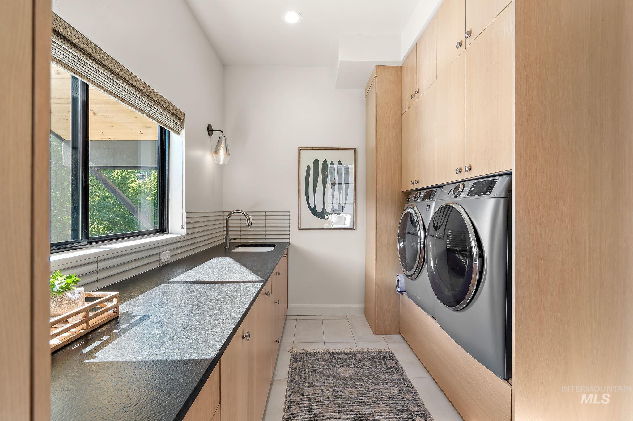 Utility room featuring extensive blonde wood cabinetry, dark-toned countertops, and a stainless steel sink with a gooseneck faucet