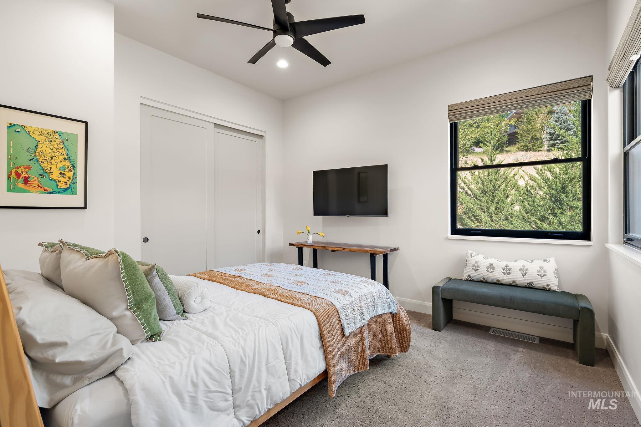 Carpeted room with a ceiling fan, dual sliding closet doors, and two windows with exterior views