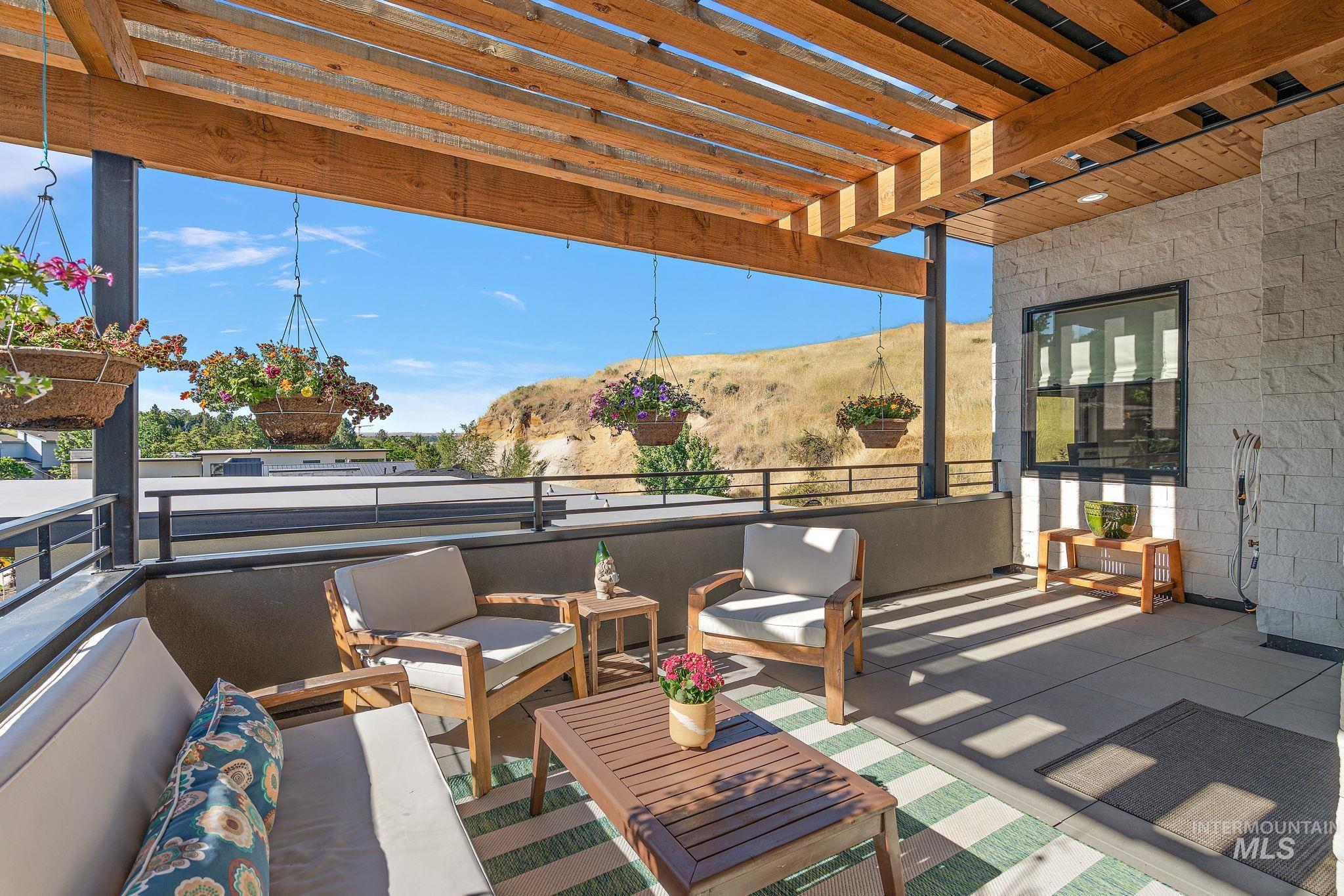 Exterior terrace featuring a wood beam pergola, stone facade, black metal railing, and concrete flooring
