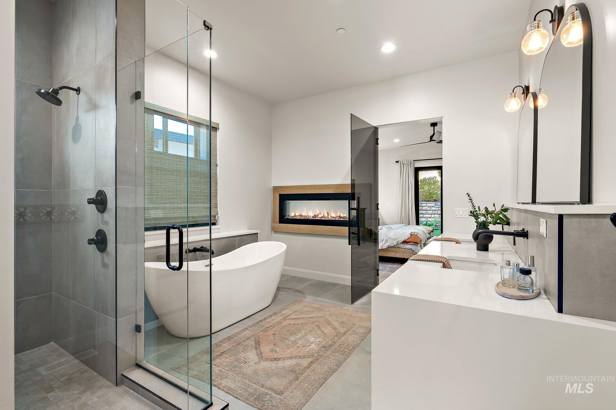 Spacious bathroom featuring a glass-enclosed shower with dark-finish fixtures, a freestanding soaking tub, a built-in linear electric fireplace, and a dual vanity with undermount sinks and dark-finish faucets