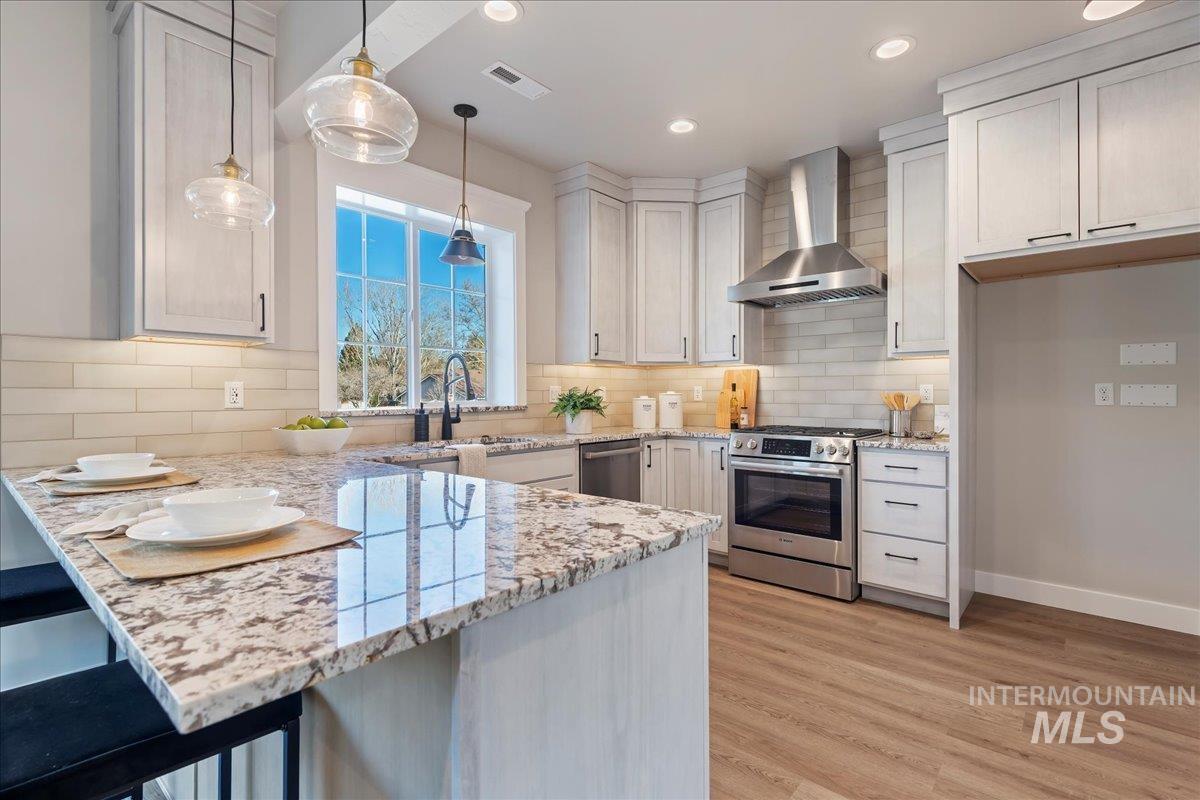Kitchen with wall chimney exhaust hood, light stone counters, appliances with stainless steel finishes, a peninsula, and hanging light fixtures