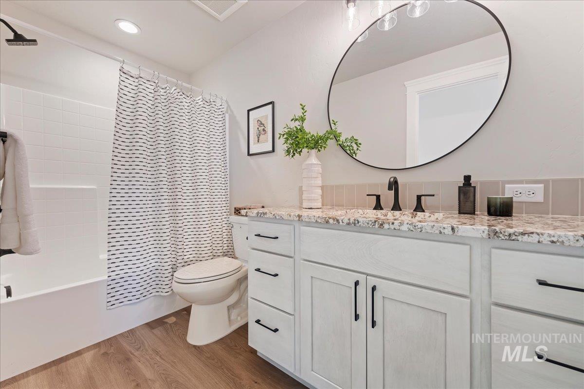 Full bath with vanity, shower / bathtub combination with curtain, and light wood-style flooring