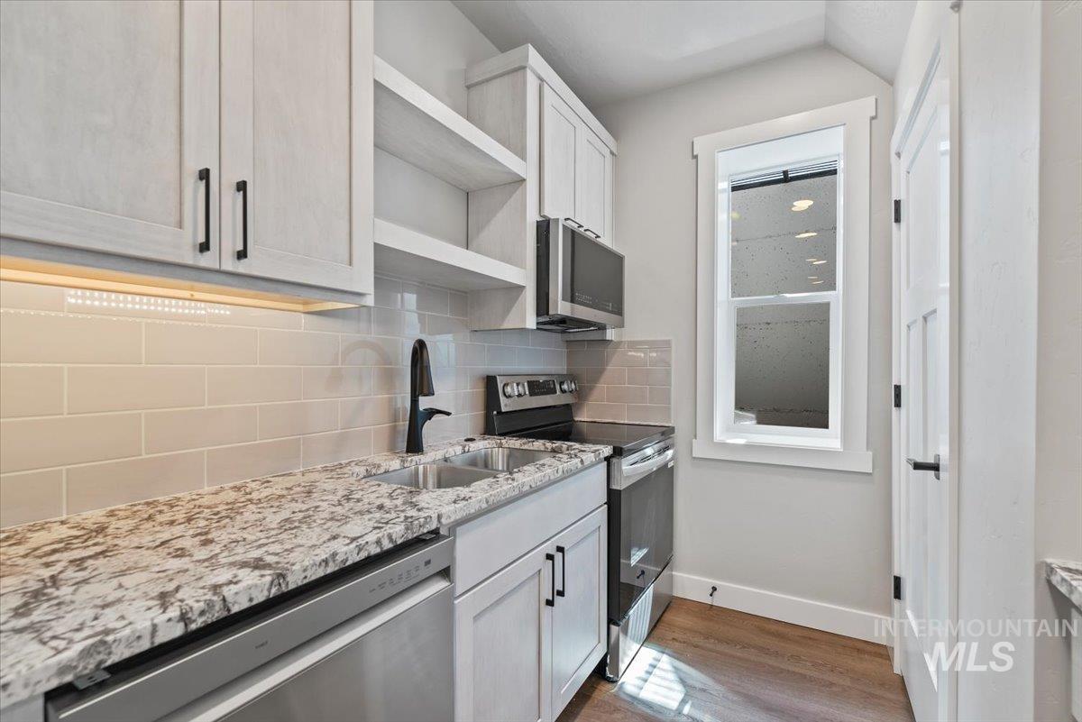 Kitchen with stainless steel appliances, open shelves, light wood LVP floors, light stone countertops, and decorative backsplash