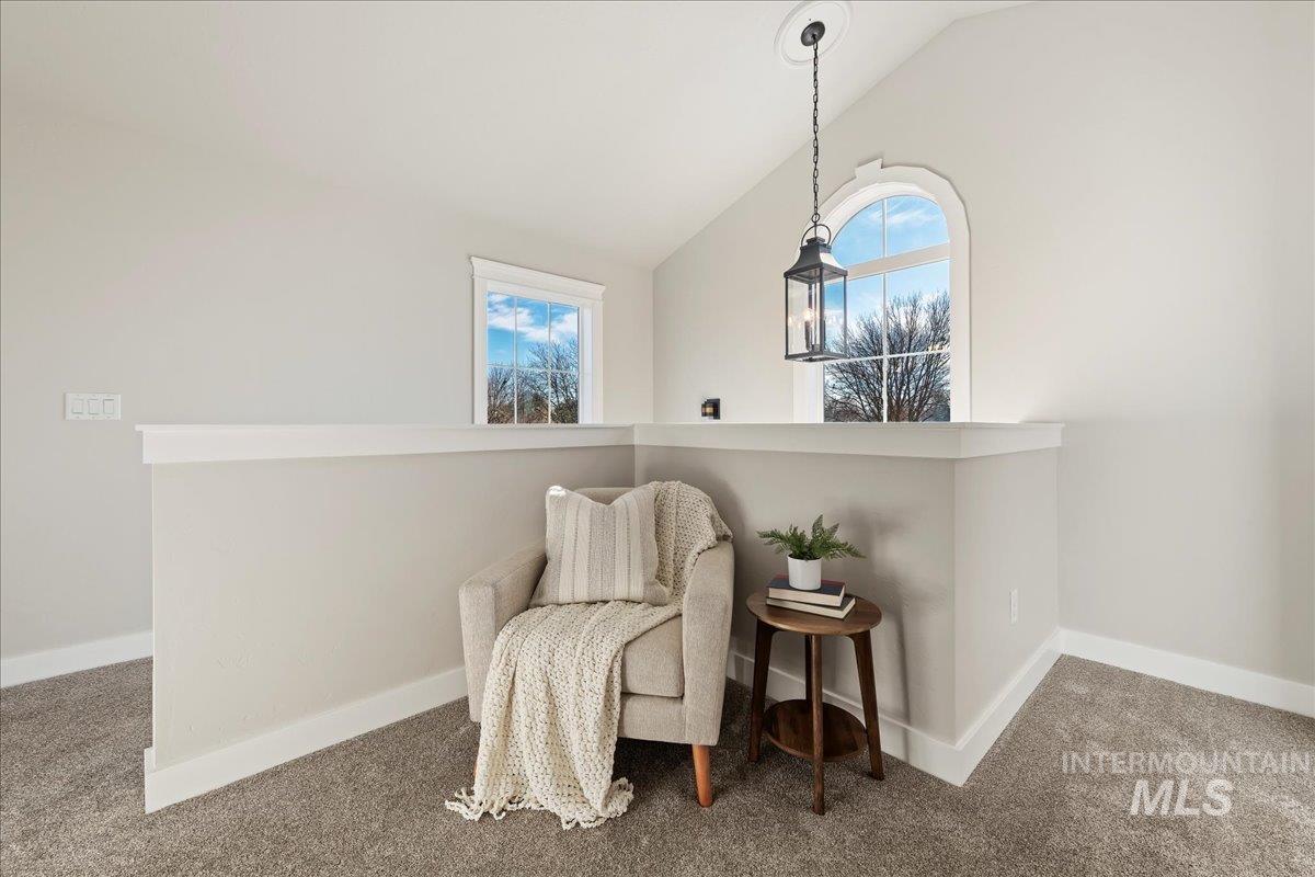 Sitting room with vaulted ceiling, plenty of natural light, an upstairs landing, and carpet floors