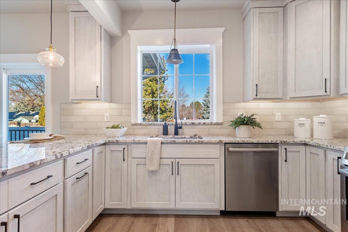 Kitchen with dishwasher, light stone counters, hanging light fixtures, and decorative backsplash