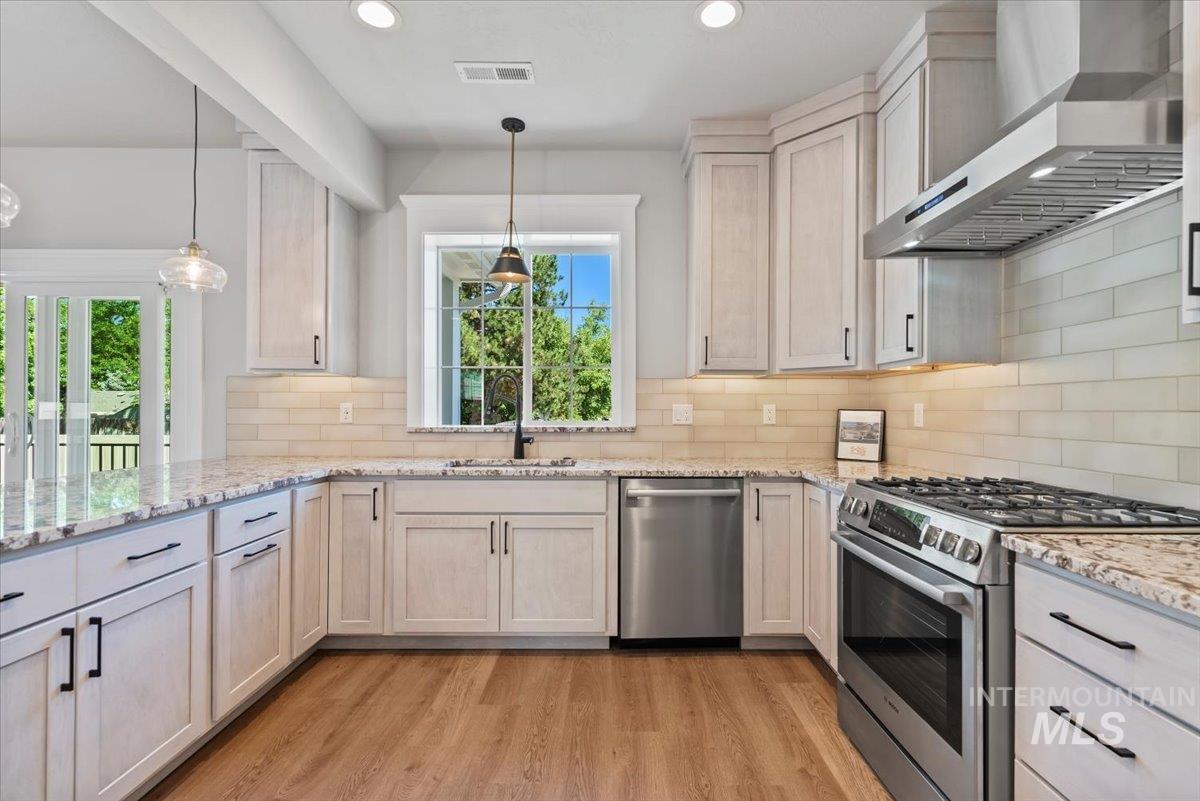 Kitchen featuring stainless steel appliances, wall chimney exhaust hood, light wood-type flooring, backsplash, and recessed lighting