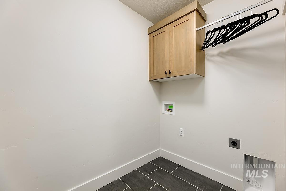 Utility room featuring wood-finish cabinetry, a chrome hanging rod, and large format tile flooring