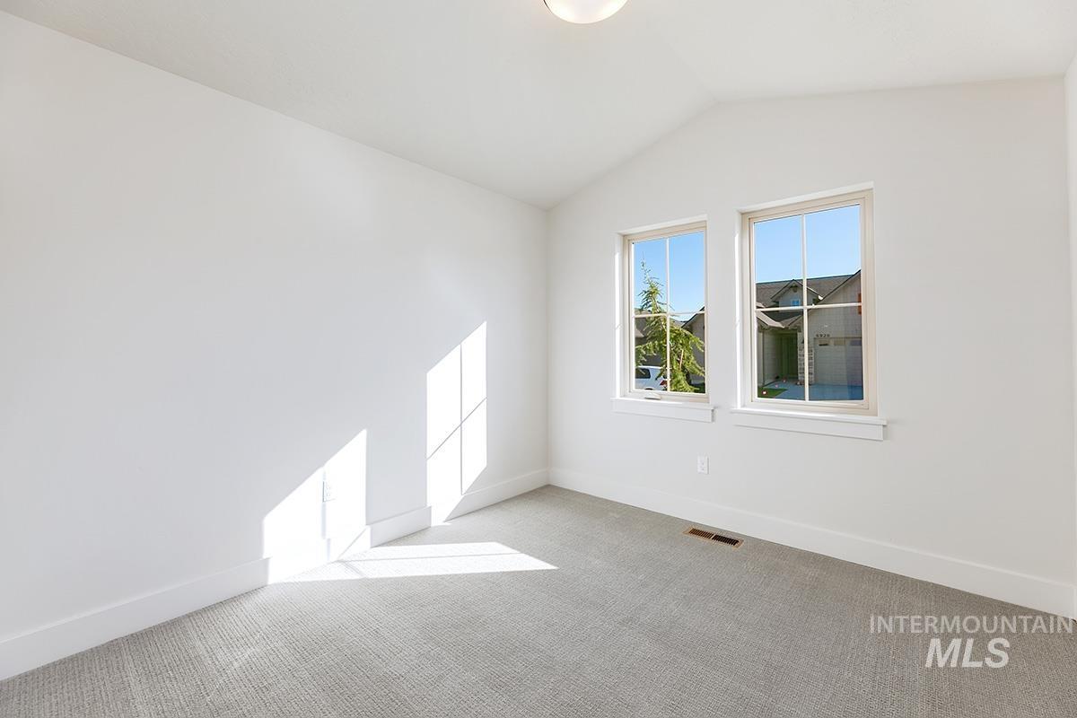 White wall finish, vaulted ceiling, two double-hung windows, light gray carpet, and white baseboards