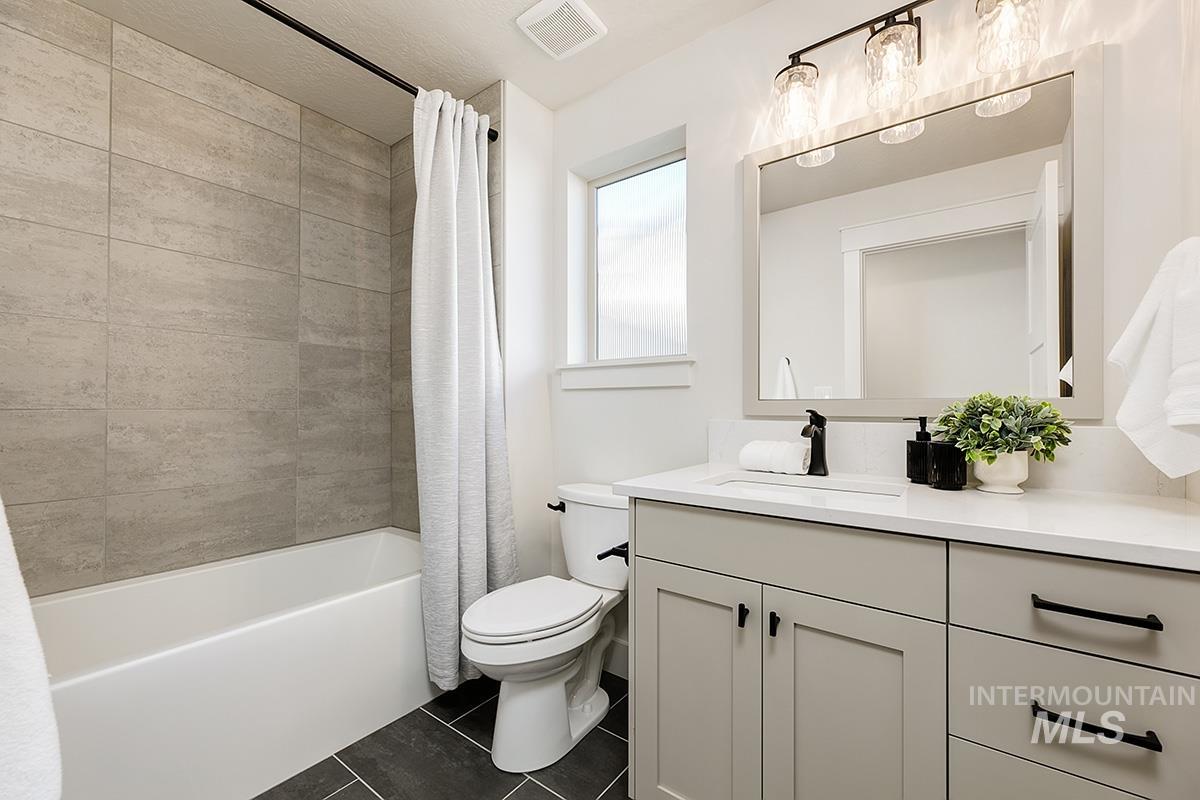 Modern bathroom featuring a white bathtub with gray tiled surround, dark tile flooring, a white toilet, and a light-toned vanity with a white countertop and rectangular undermount sink