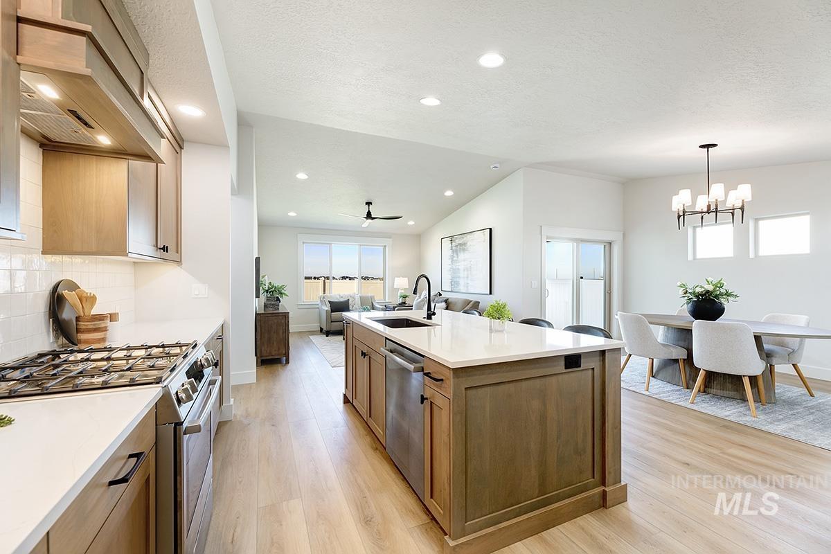 Gourmet kitchen featuring a gas range, white subway tile backsplash, light wood-finish flooring, and a central island with a built-in sink and dishwasher