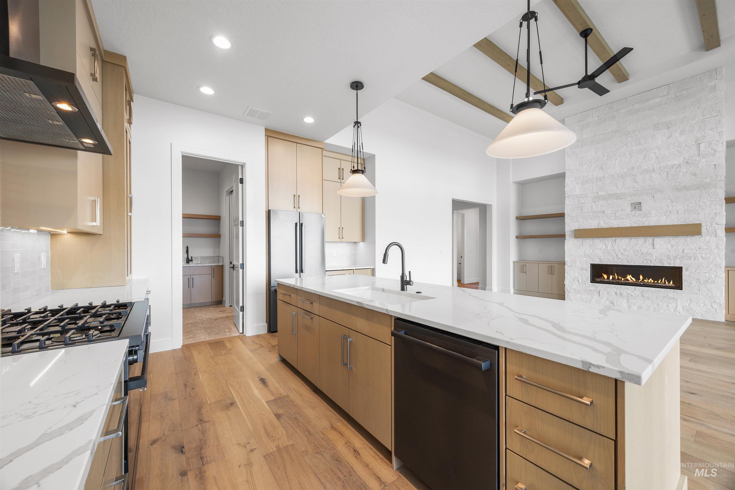 Kitchen with light wood-type flooring, light stone counters, wall chimney range hood, stainless steel appliances, and hanging light fixtures