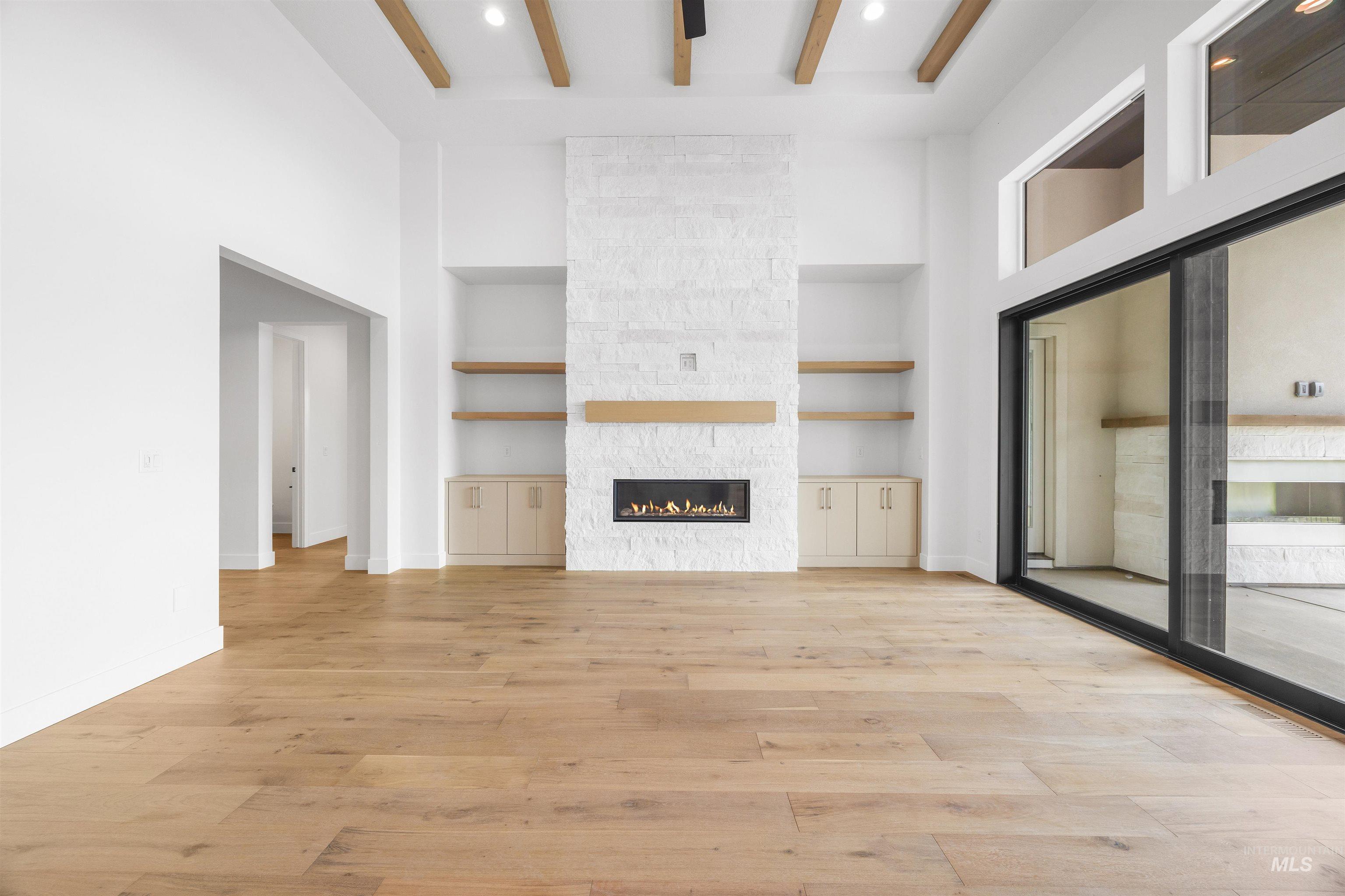 Unfurnished living room featuring built in features, light wood-style floors, a stone fireplace, and beamed ceiling
