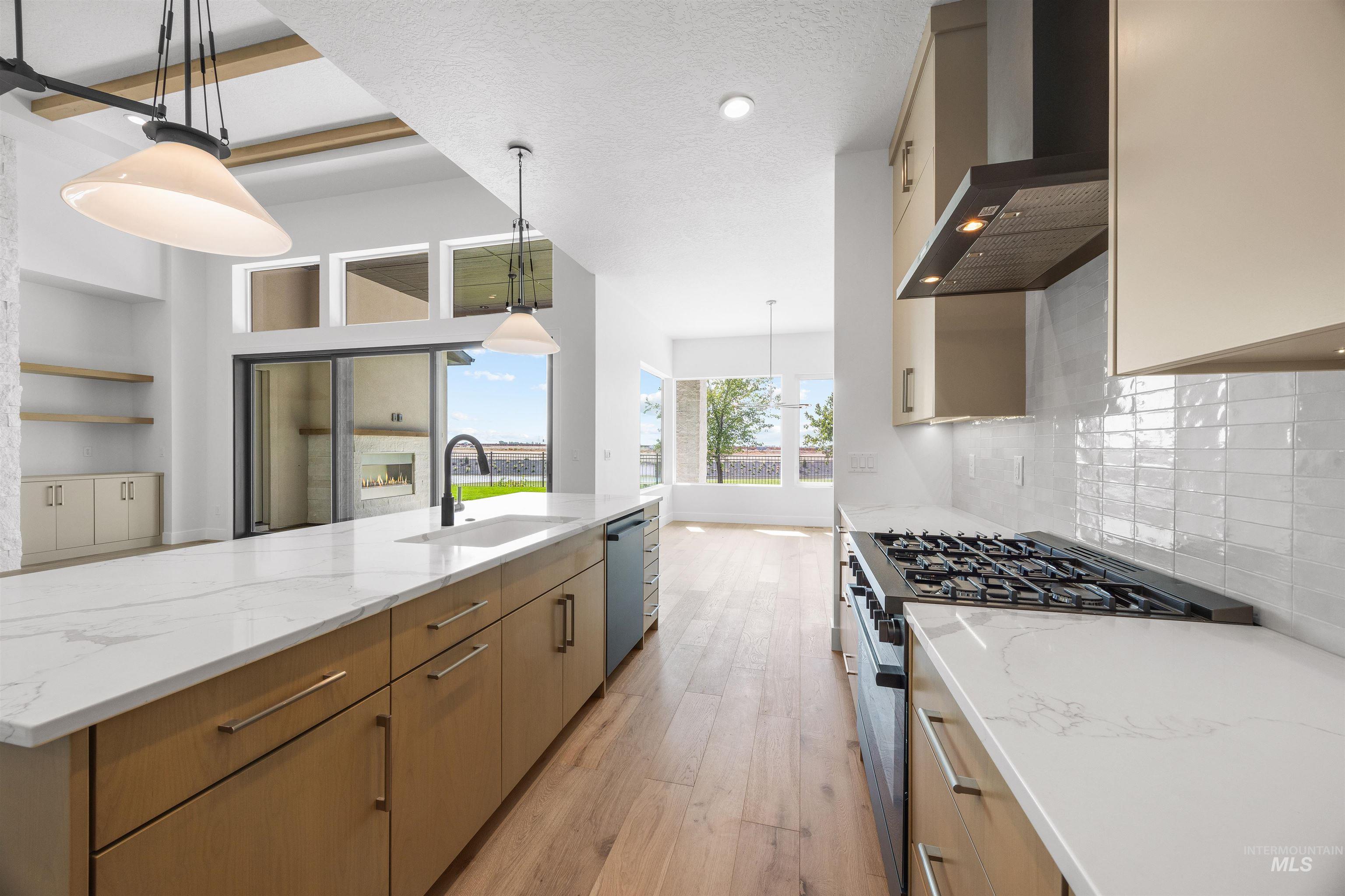 Kitchen with light stone counters, appliances with stainless steel finishes, pendant lighting, a spacious island, and a textured ceiling