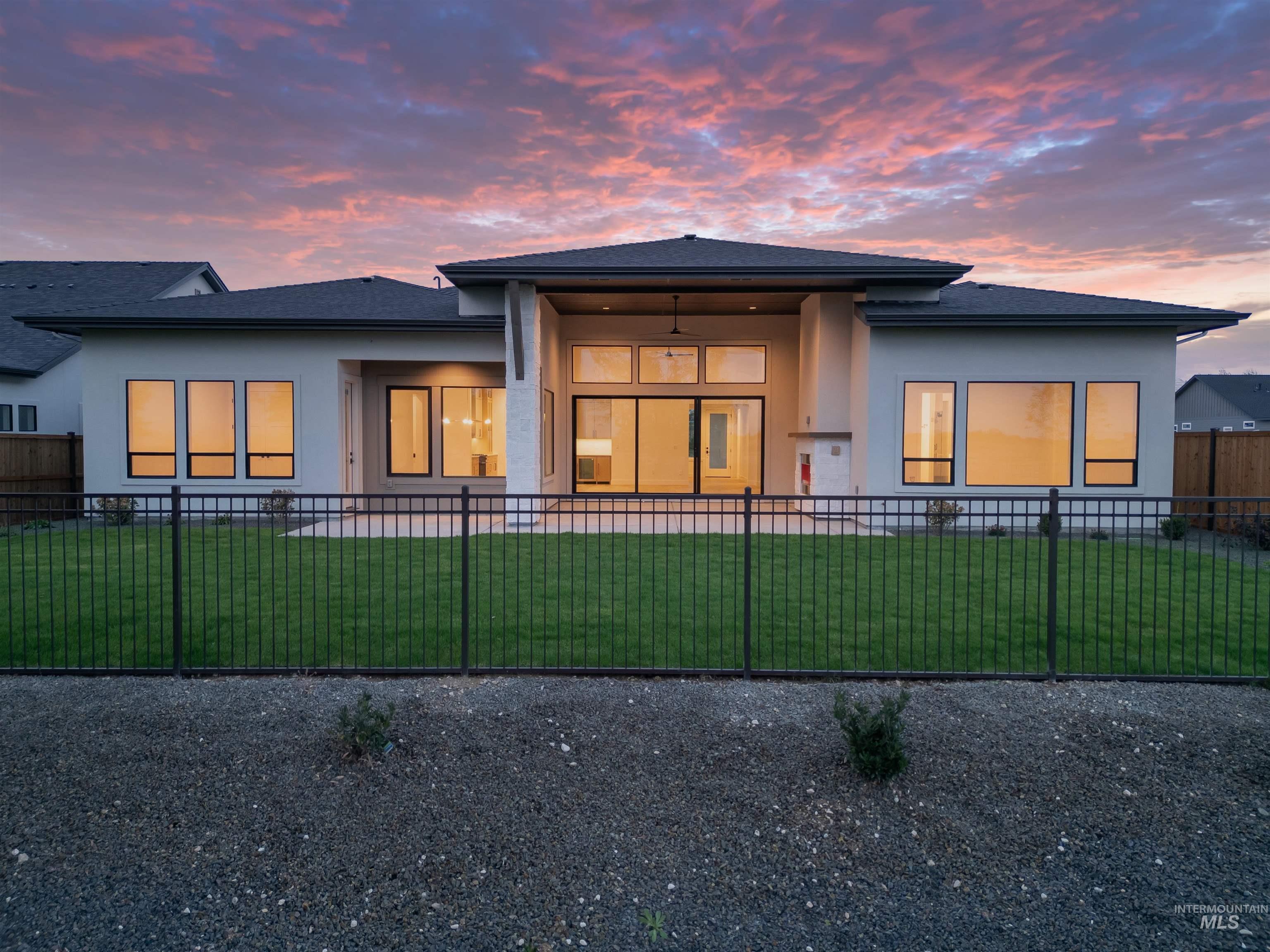 Back of property at dusk with stucco siding, a fenced front yard, a patio, and a shingled roof