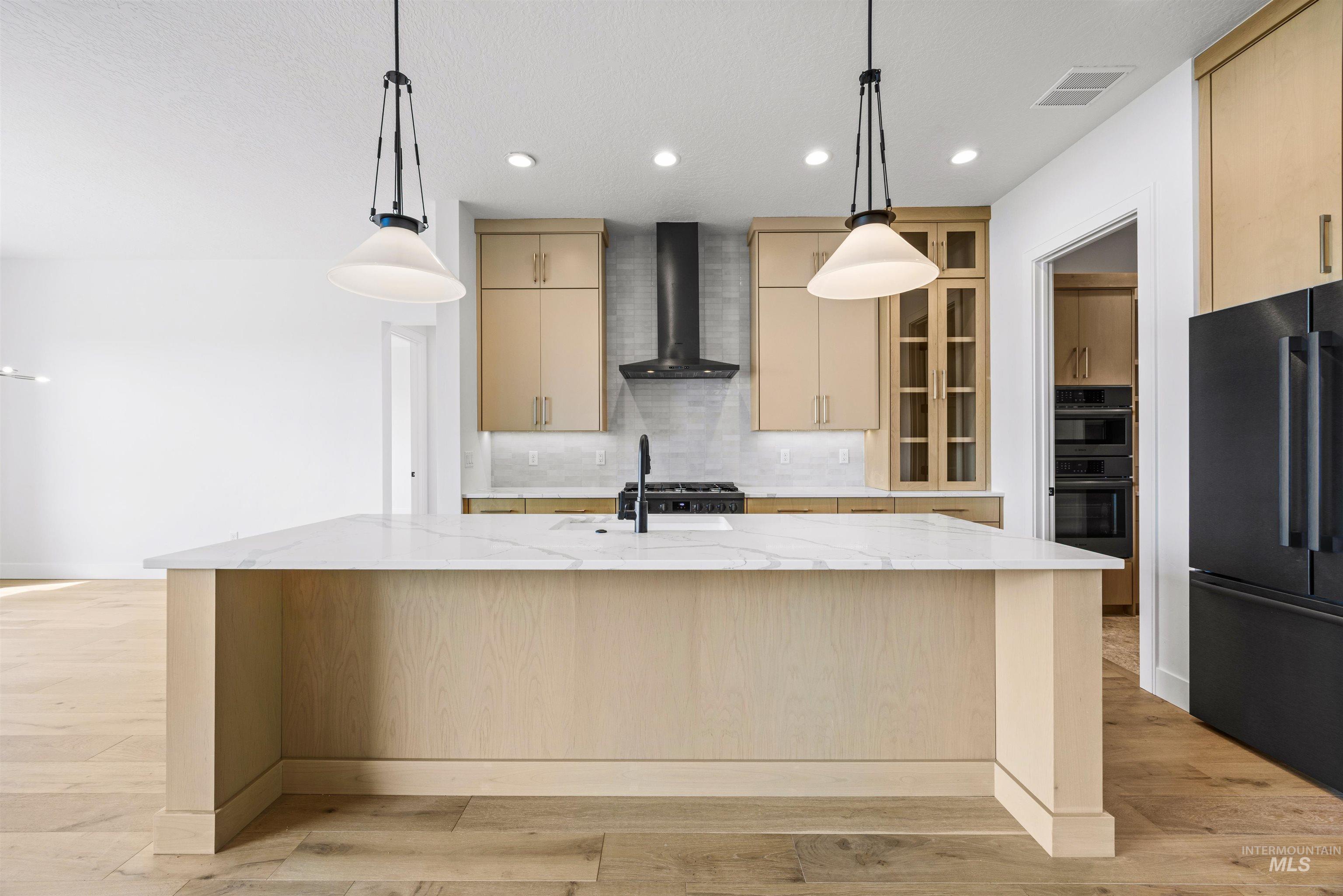 Kitchen with hanging light fixtures, light stone counters, decorative backsplash, light wood-style floors, and recessed lighting