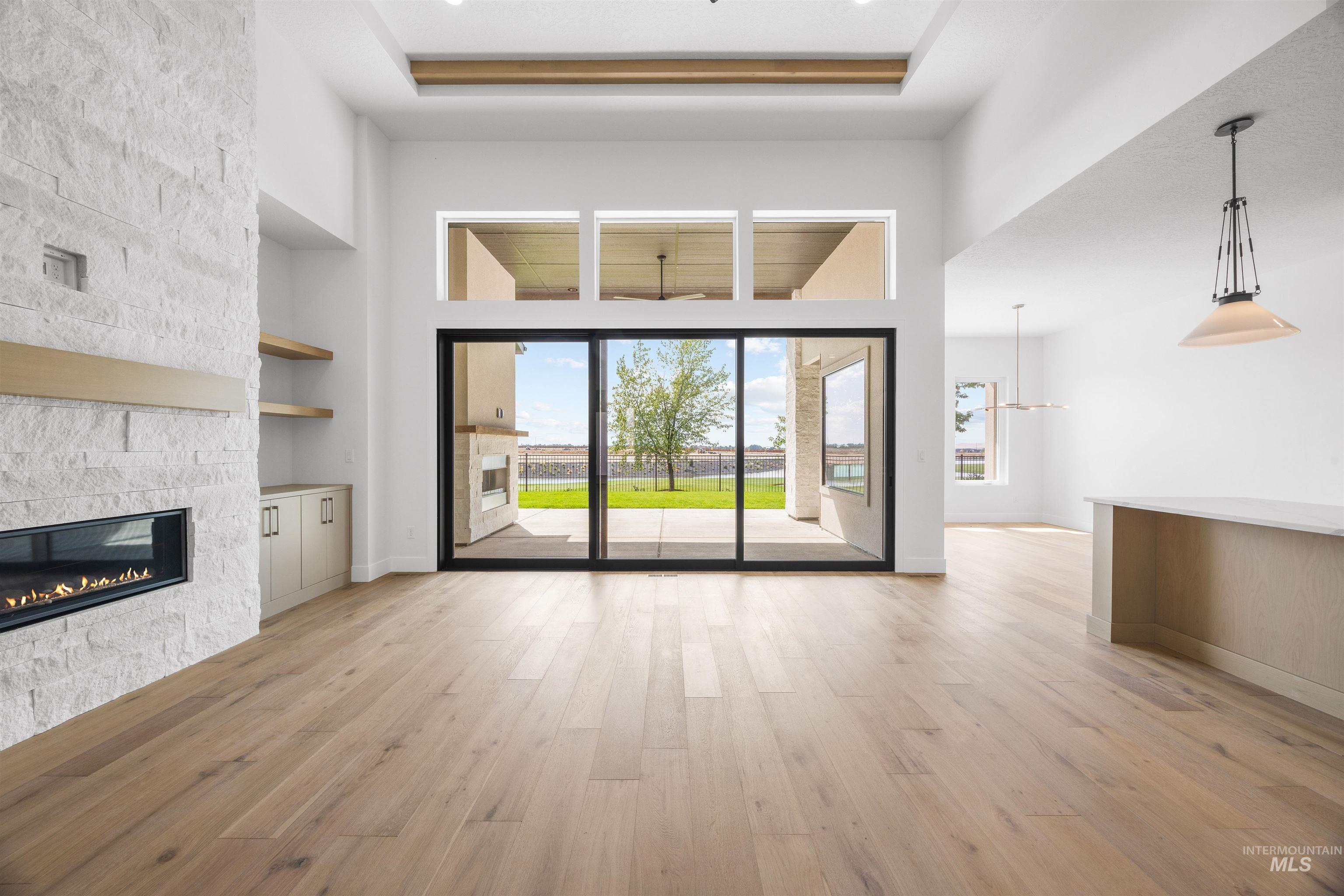 Unfurnished living room featuring light wood-type flooring, a raised ceiling, a high ceiling, a fireplace, and built in shelves