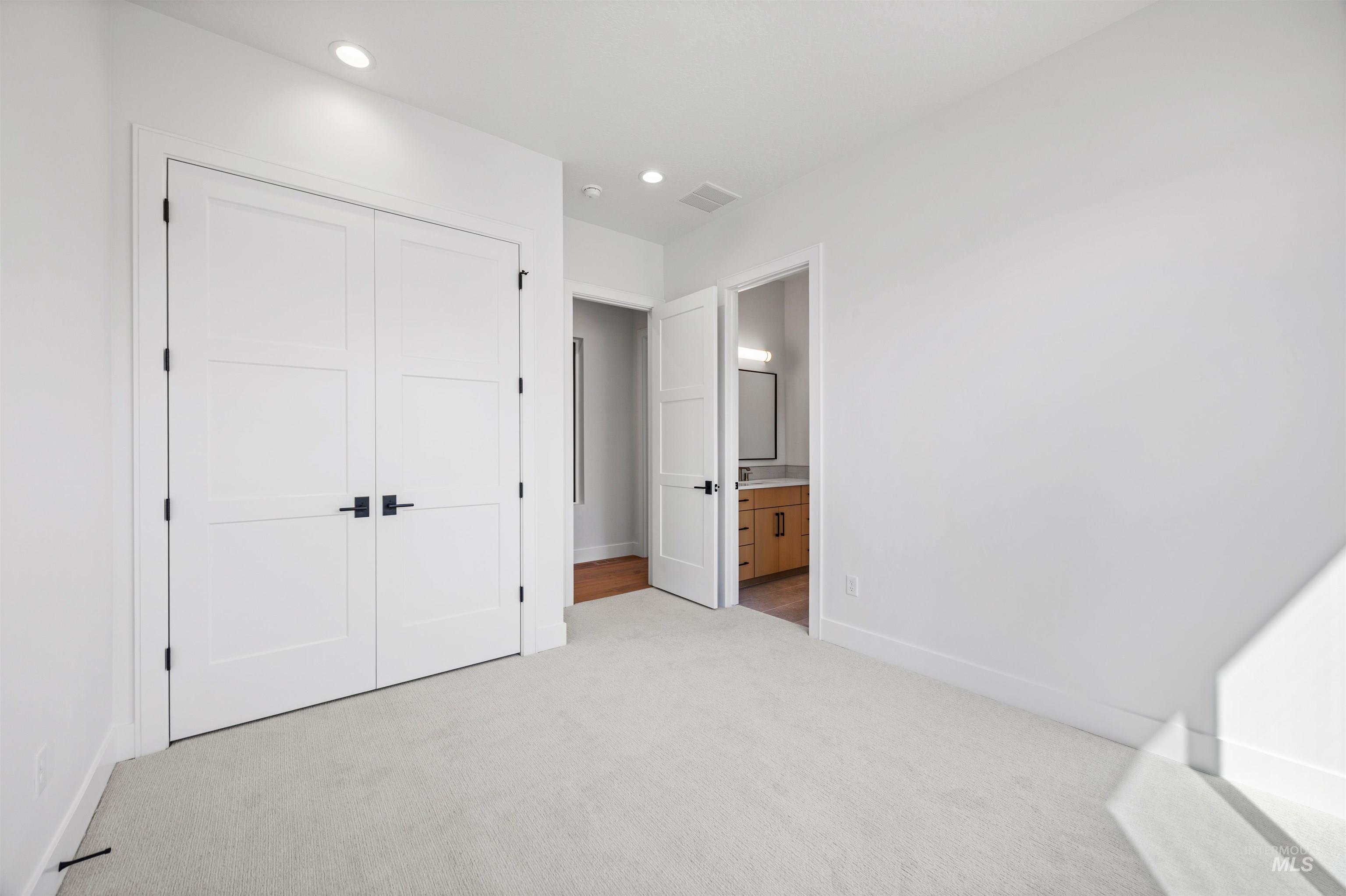 Unfurnished bedroom featuring light carpet, recessed lighting, a closet, and ensuite bathroom