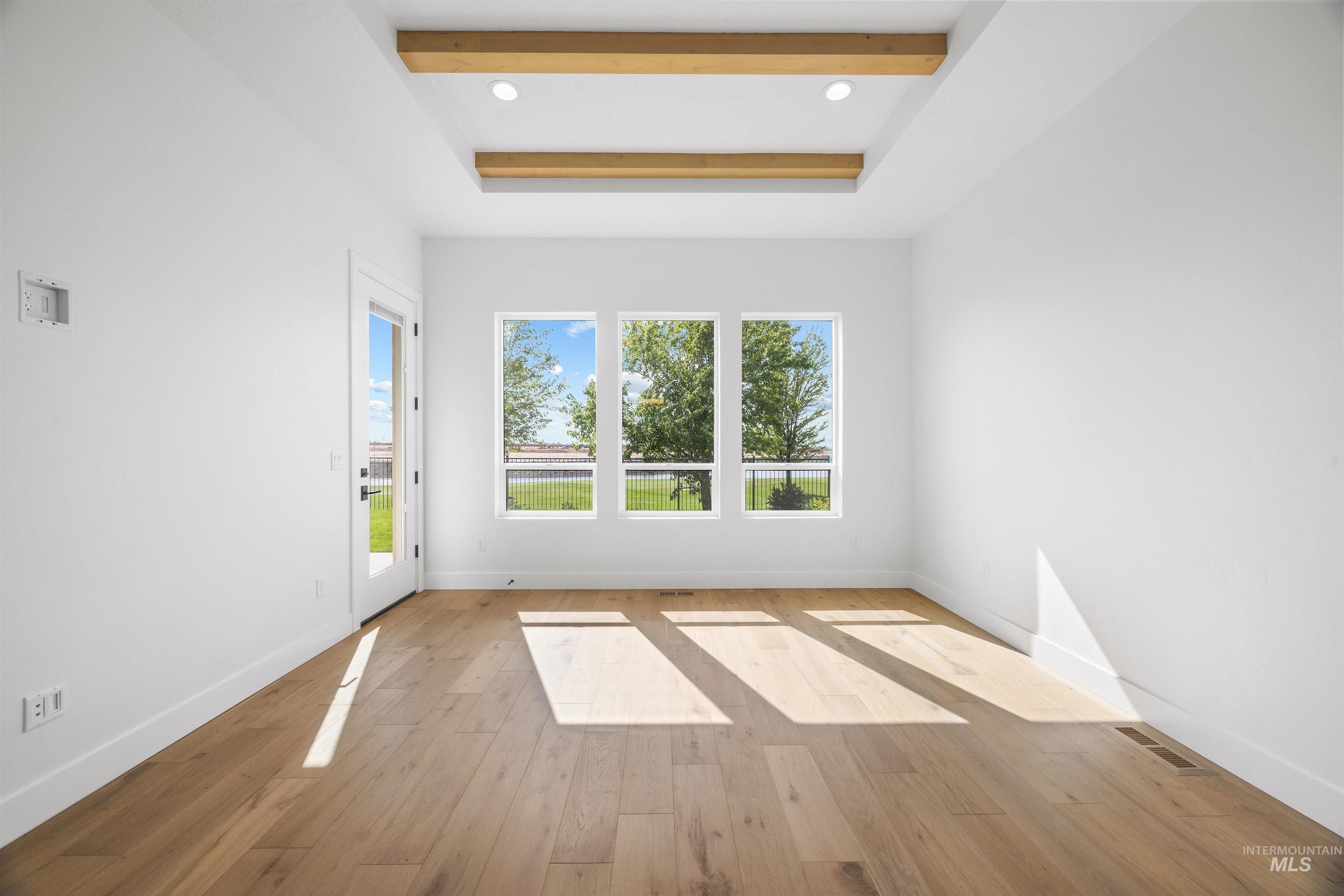 Unfurnished room featuring beamed ceiling, light wood-style flooring, a raised ceiling, and recessed lighting