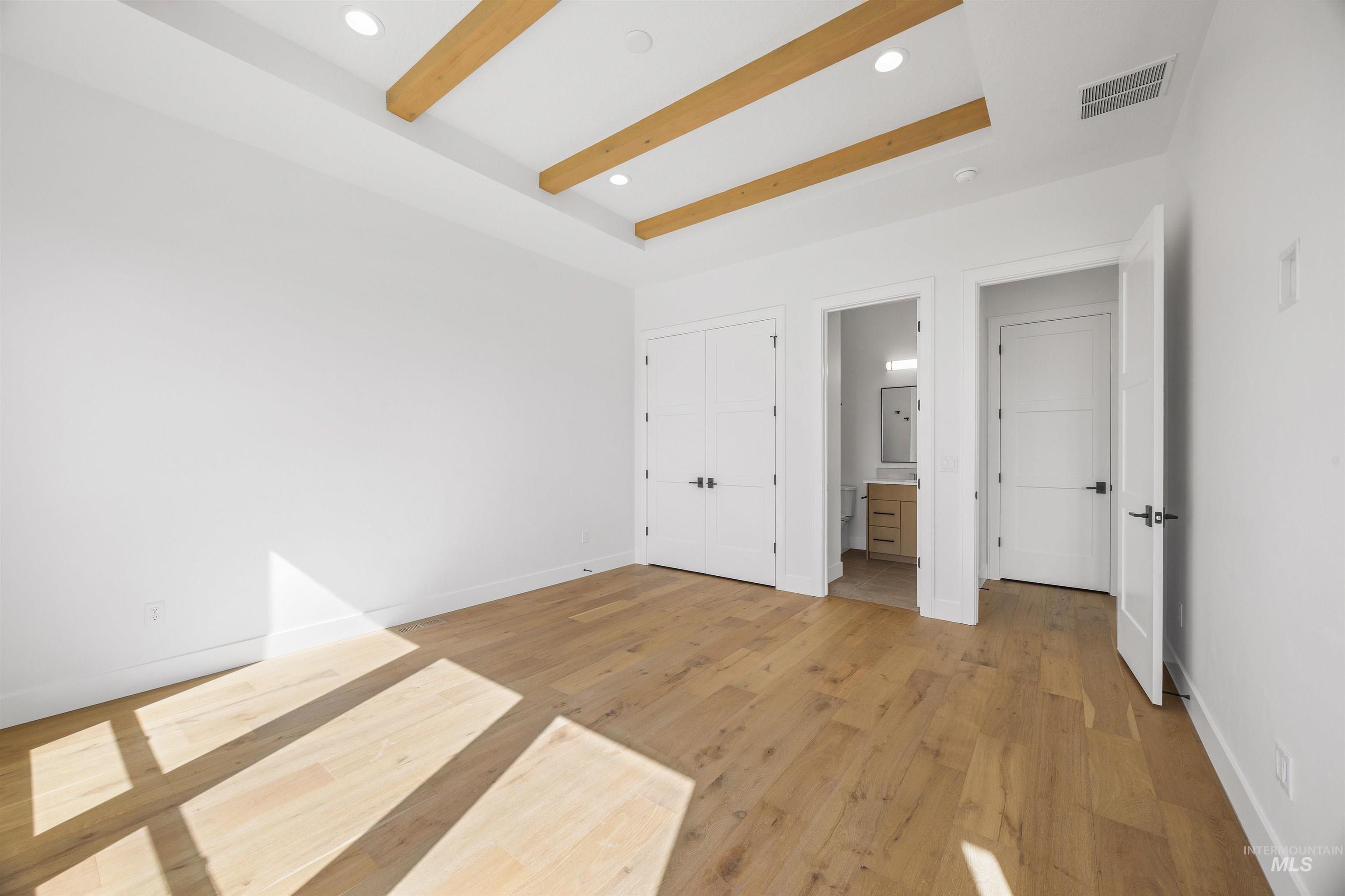 Unfurnished bedroom featuring light wood-style flooring, recessed lighting, a closet, connected bathroom, and beamed ceiling