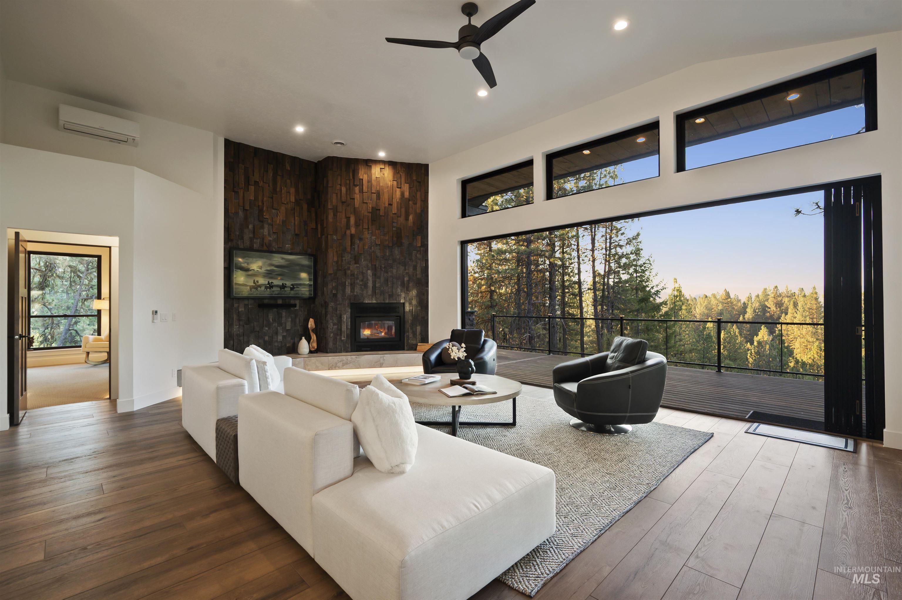 Living area featuring a ceiling fan, wood finished floors, a fireplace, a towering ceiling, and a wall mounted air conditioner
