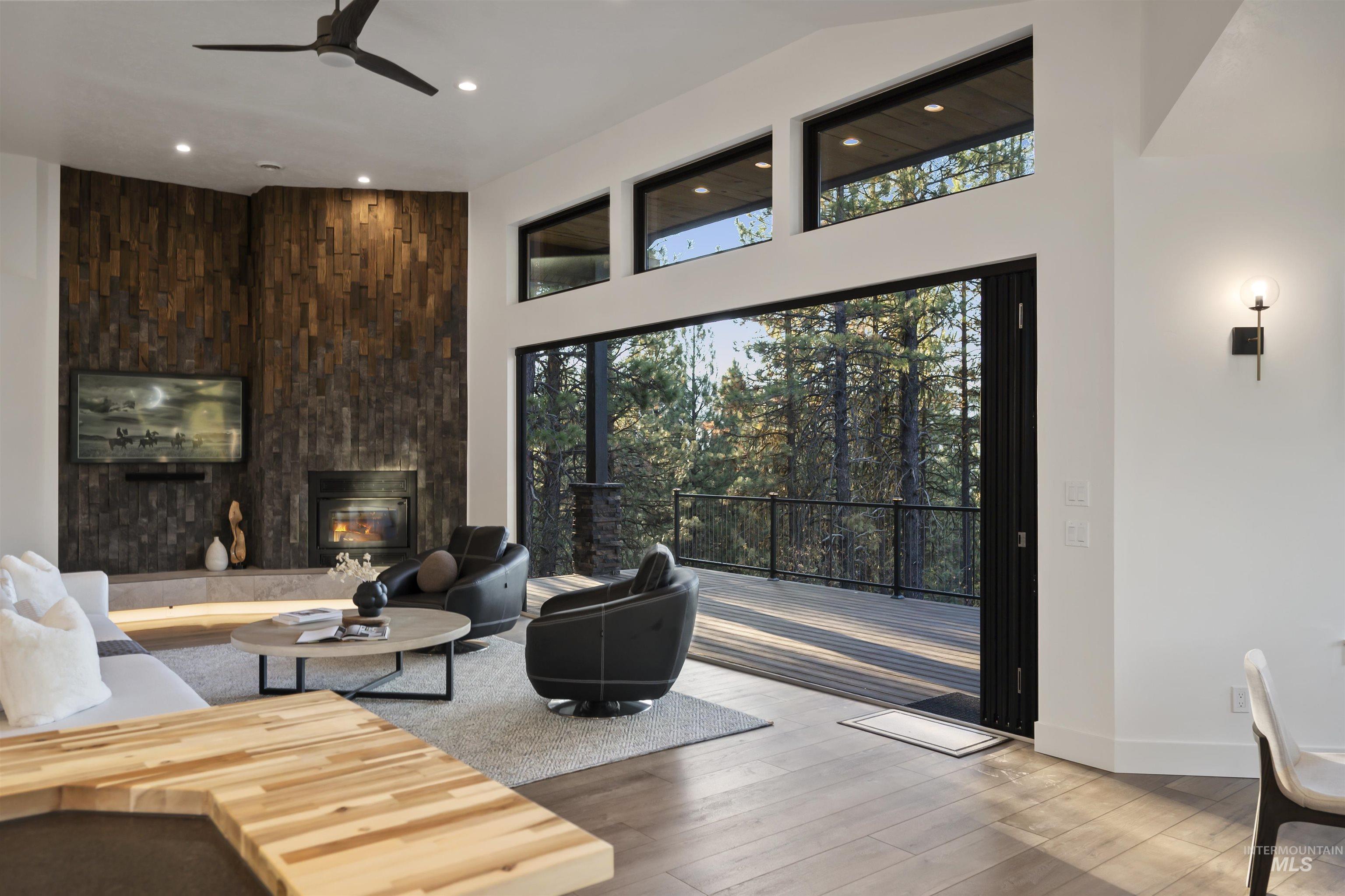 Living room featuring wood finished floors, ceiling fan, a fireplace, recessed lighting, and a towering ceiling