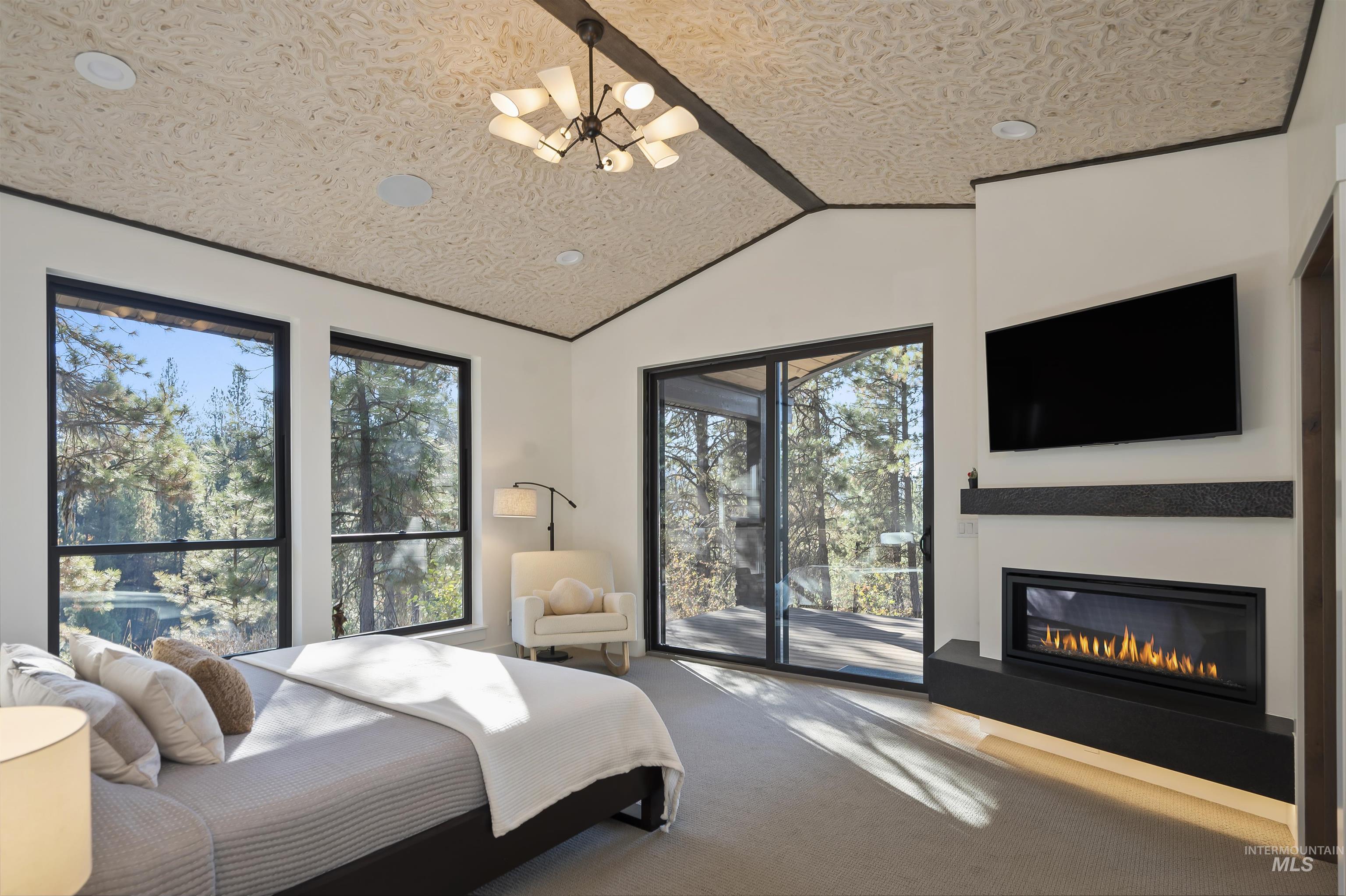 Bedroom with access to outside, carpet, a chandelier, lofted ceiling, and a glass covered fireplace
