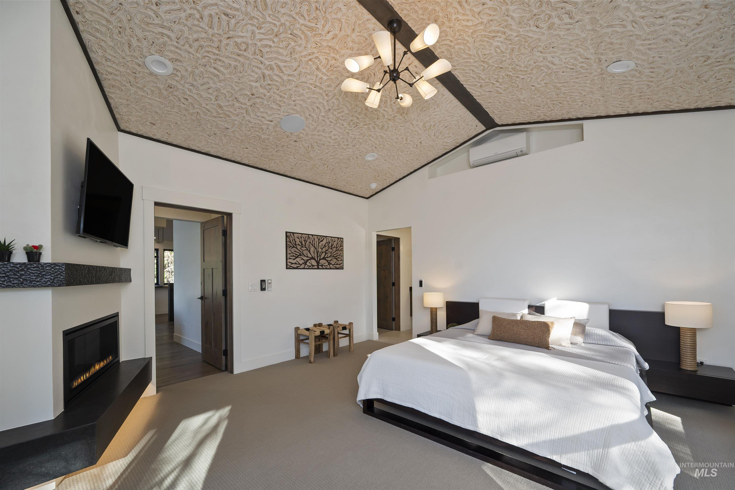 Bedroom with a chandelier, vaulted ceiling, carpet floors, a glass covered fireplace, and a wall unit AC