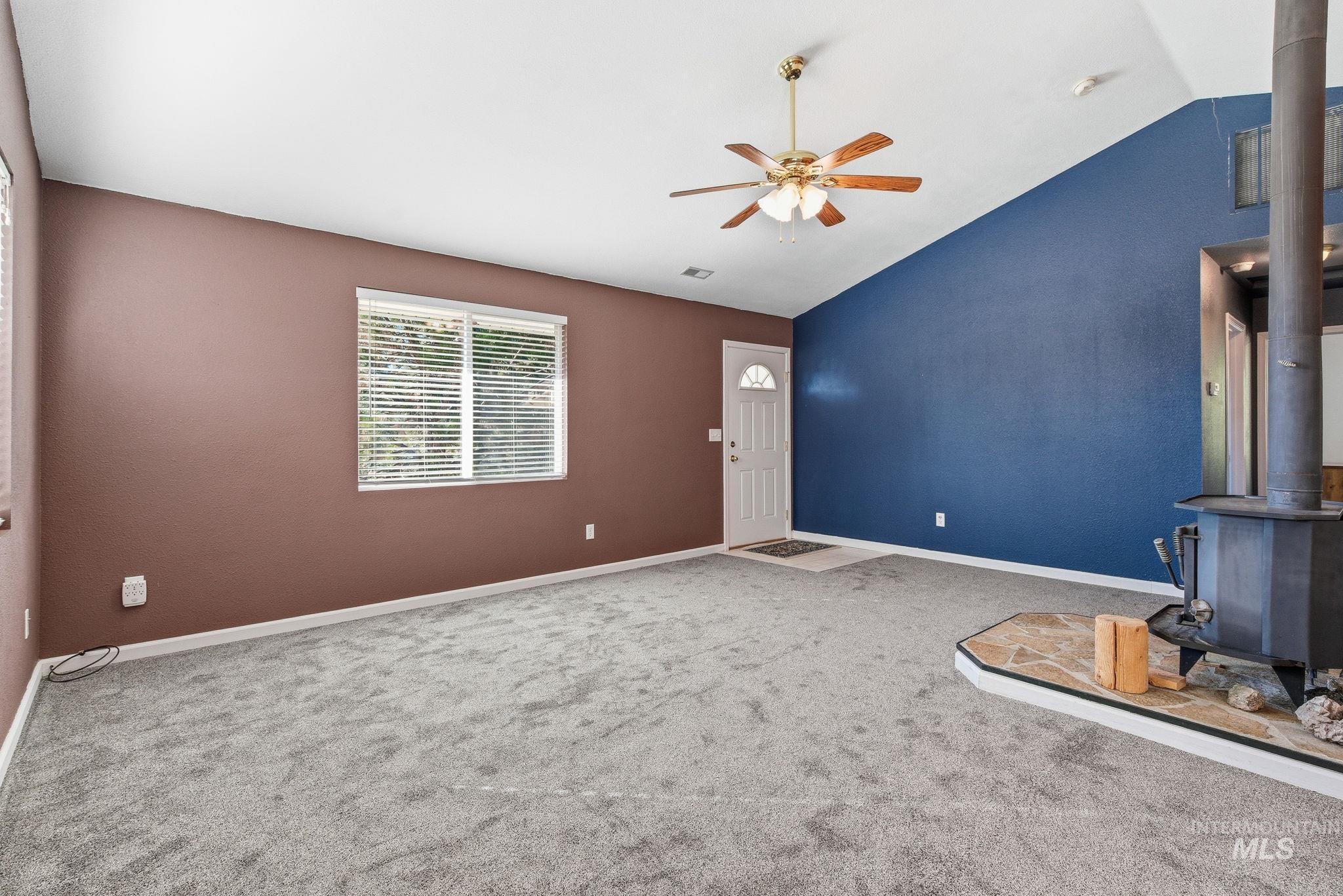Unfurnished living room with a wood stove, vaulted ceiling, carpet flooring, and a ceiling fan