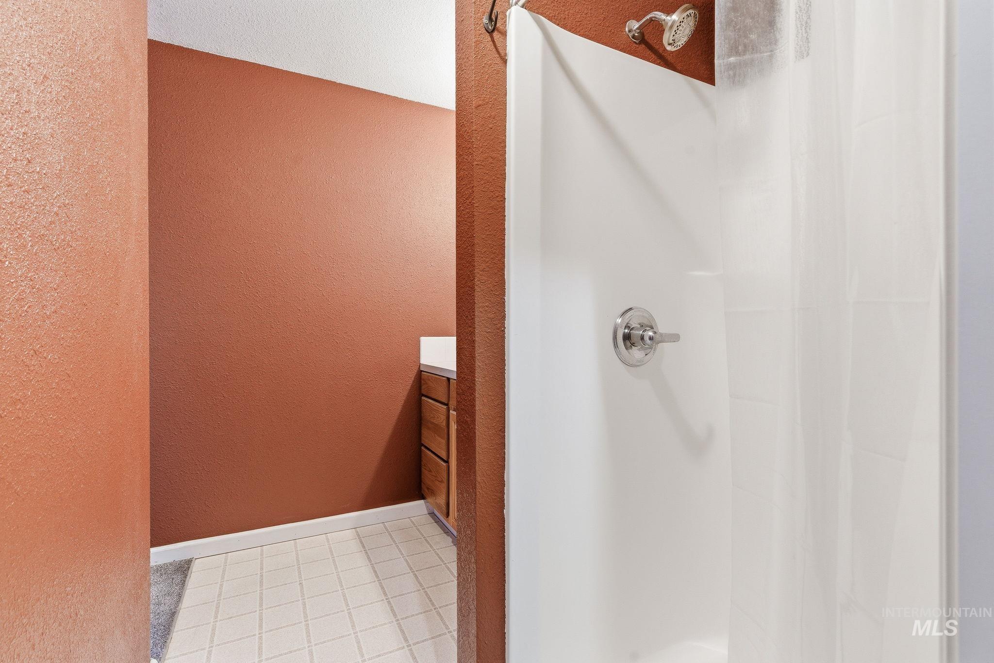 Bathroom featuring a textured wall, vanity, a shower with curtain, and light tile patterned floors