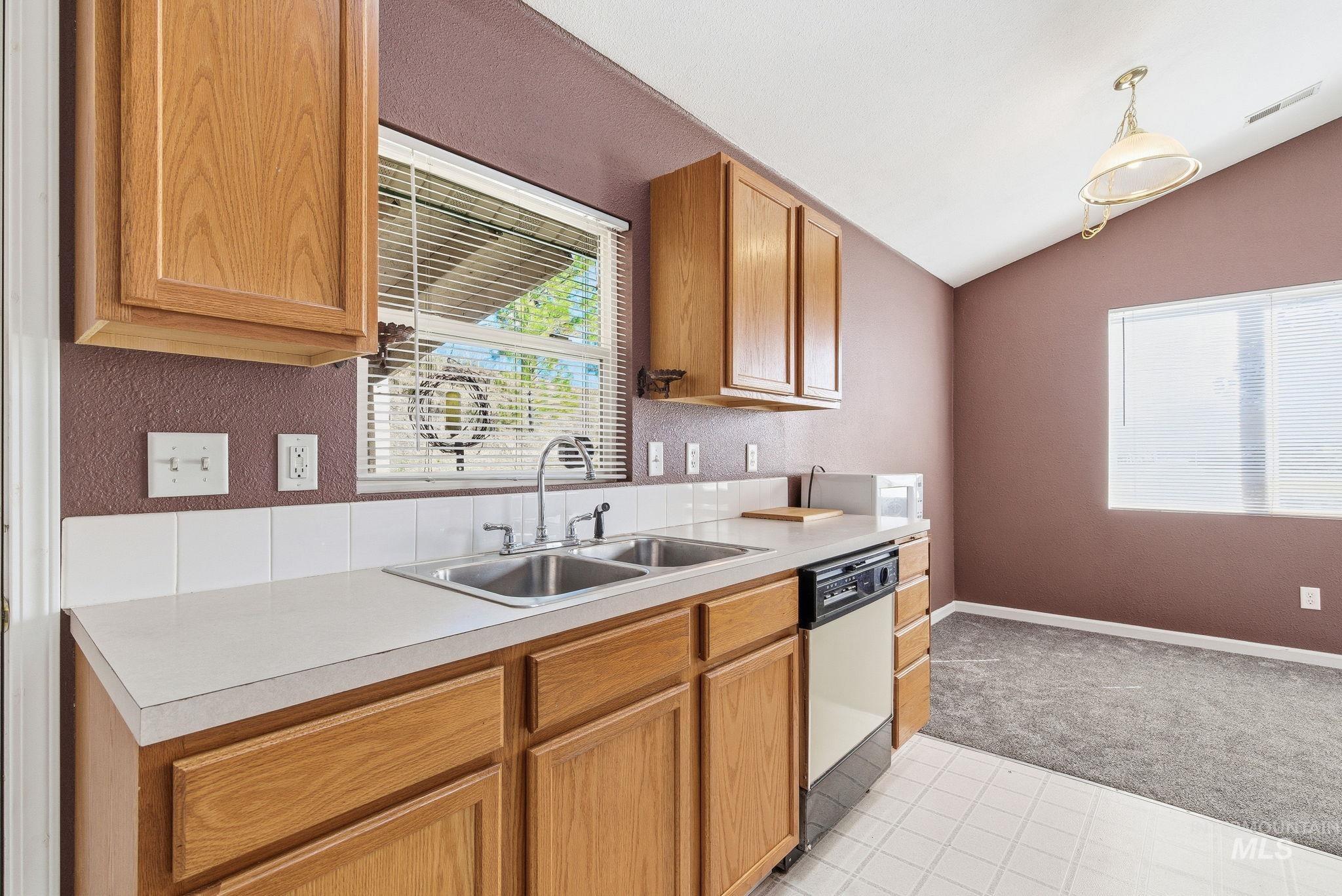 Kitchen with vaulted ceiling, light countertops, dishwasher, brown cabinets, and decorative light fixtures