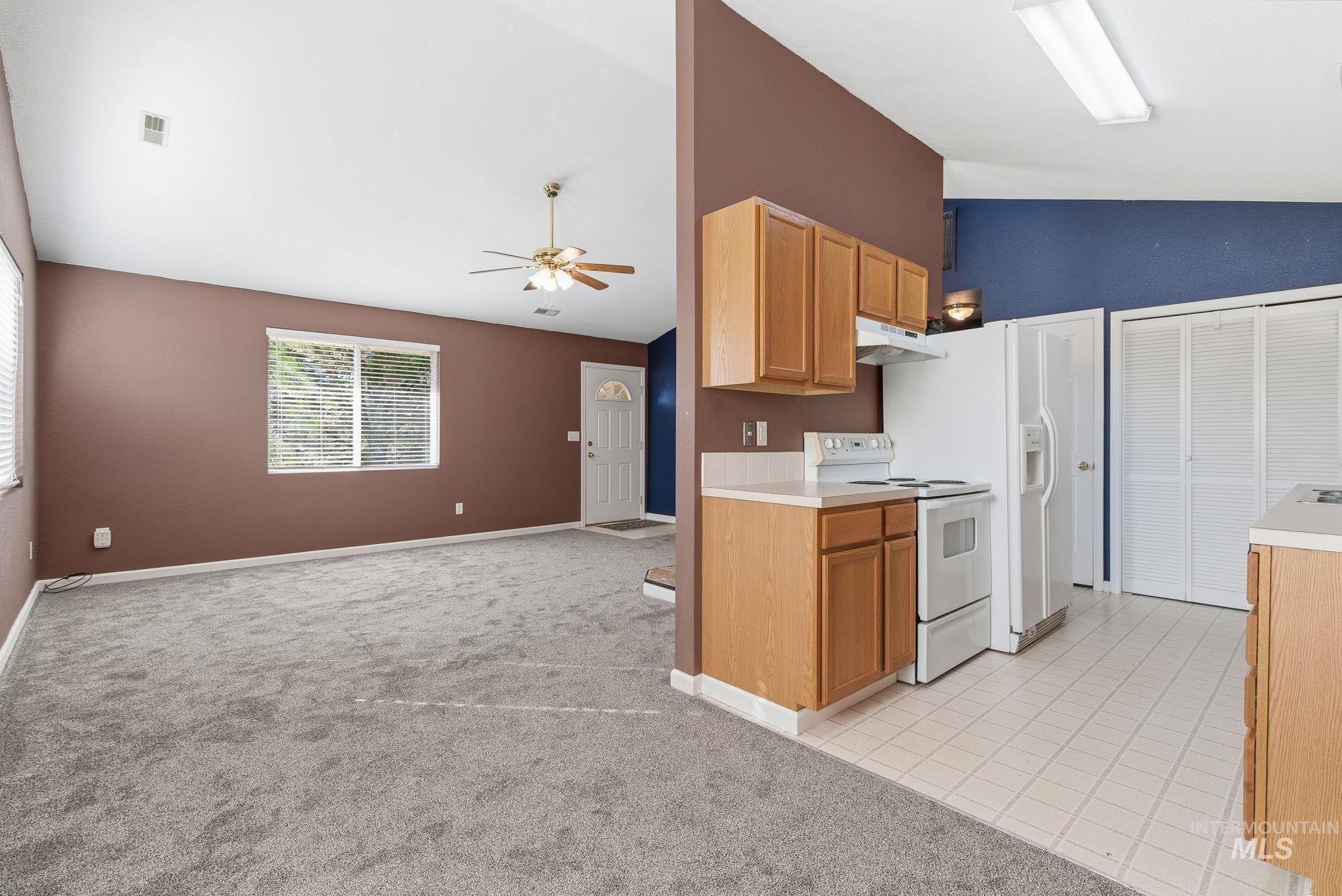 Kitchen with lofted ceiling, white range with electric cooktop, open floor plan, light countertops, and light colored carpet