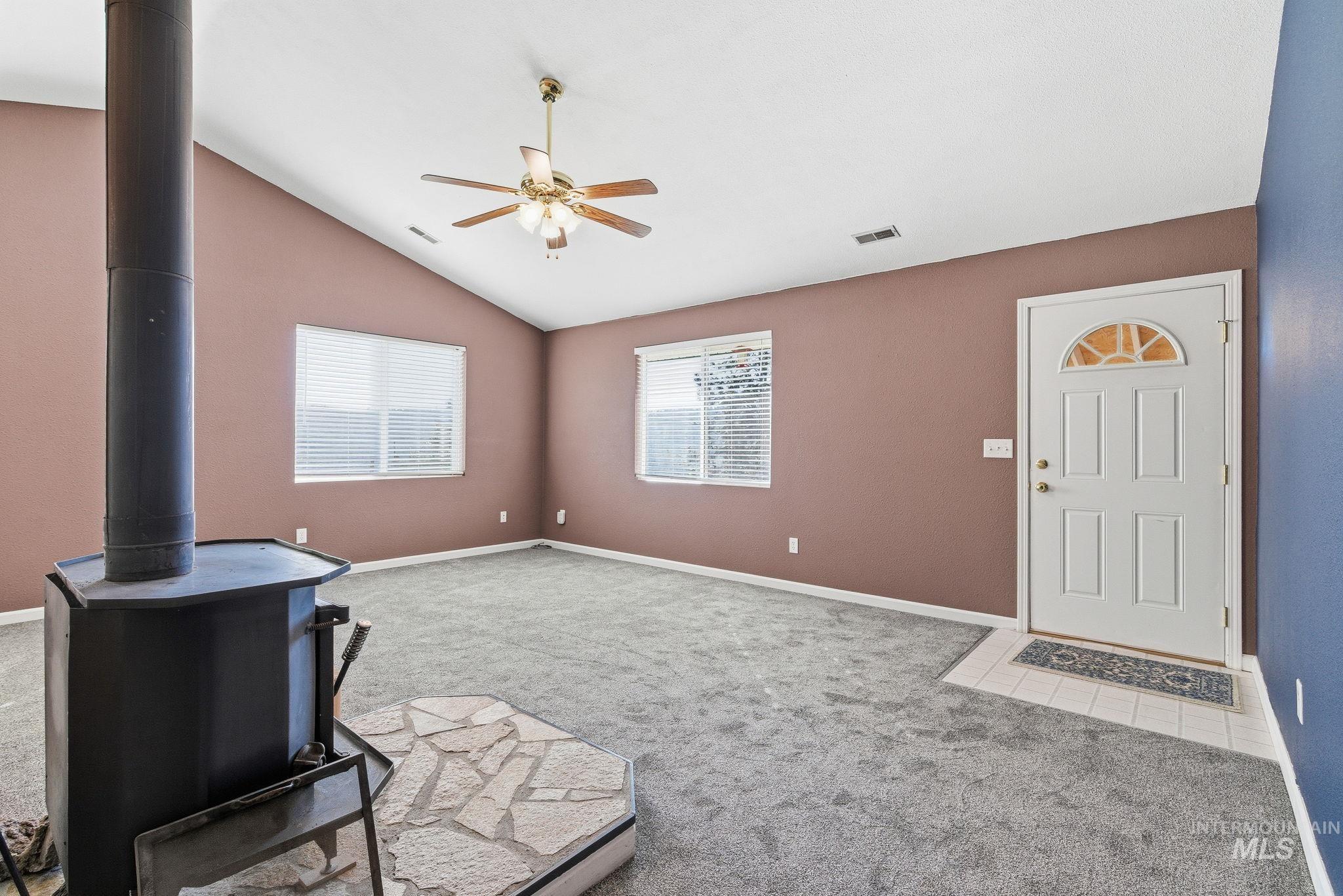 Unfurnished living room with vaulted ceiling, light colored carpet, a wood stove, and ceiling fan