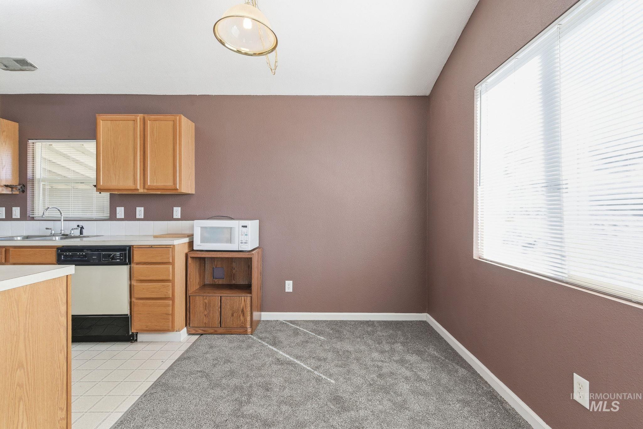Kitchen featuring light countertops, white appliances, lofted ceiling, light tile patterned floors, and light carpet