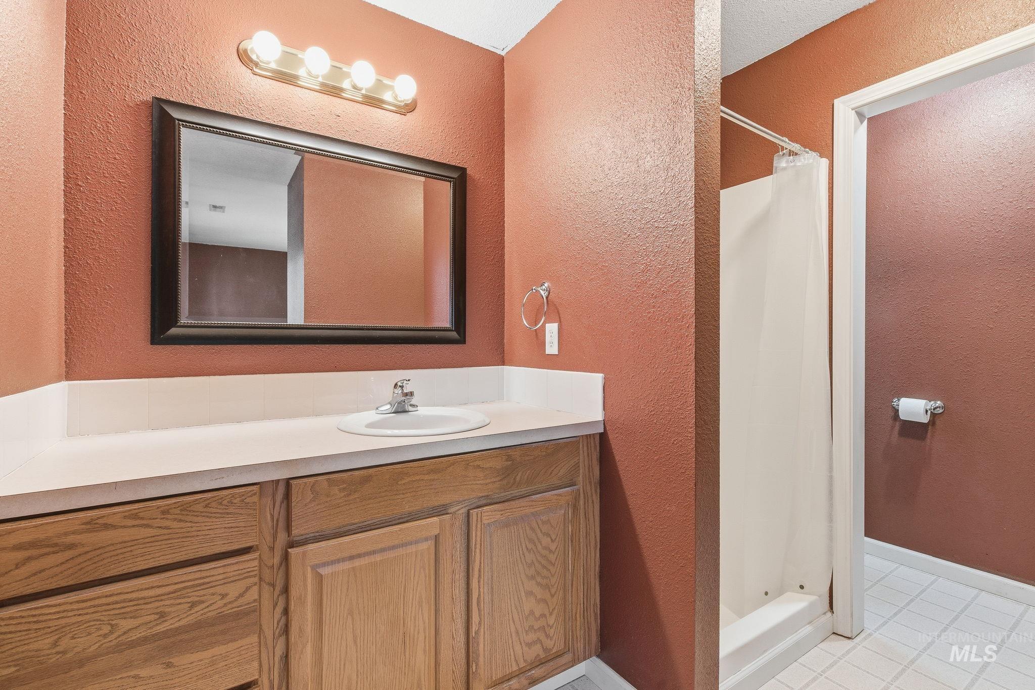 Full bath with a textured wall, a stall shower, light tile patterned floors, and vanity