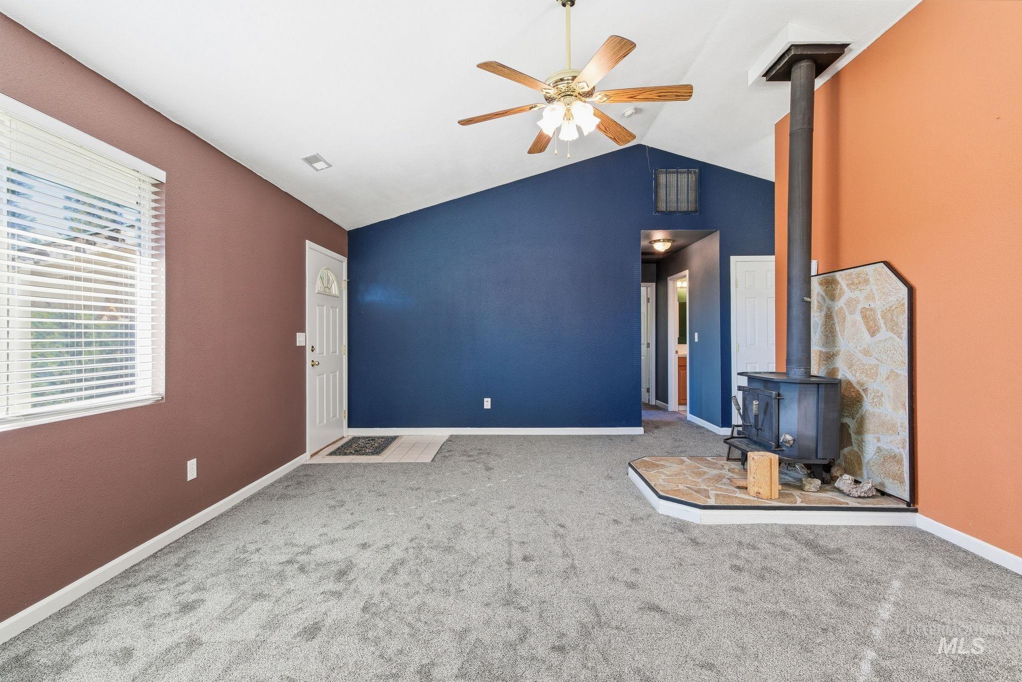 Unfurnished living room with a wood stove, carpet, a ceiling fan, and high vaulted ceiling