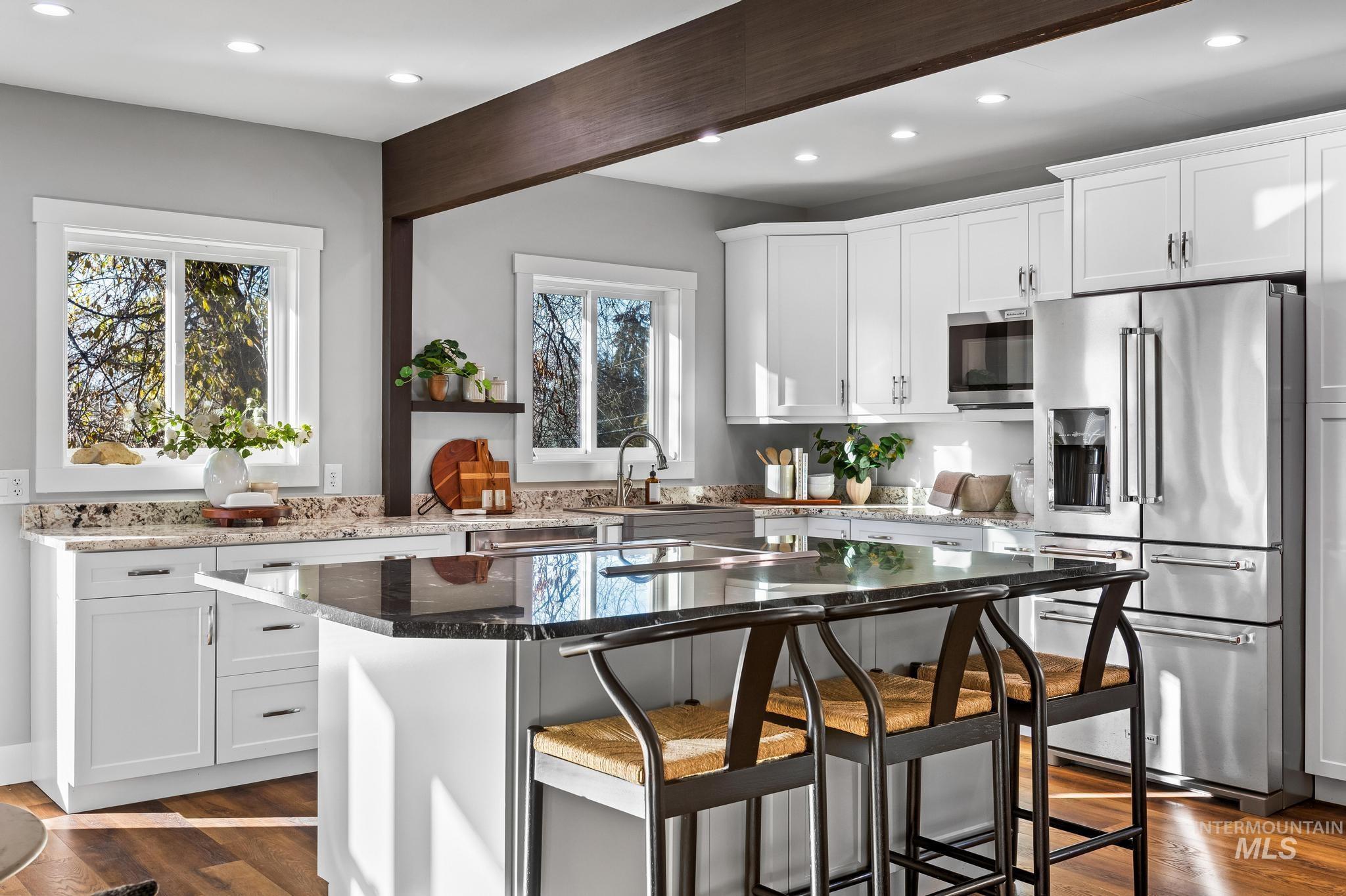 Kitchen with appliances with stainless steel finishes, dark stone countertops, white cabinetry, a breakfast bar area, and dark wood finished floors