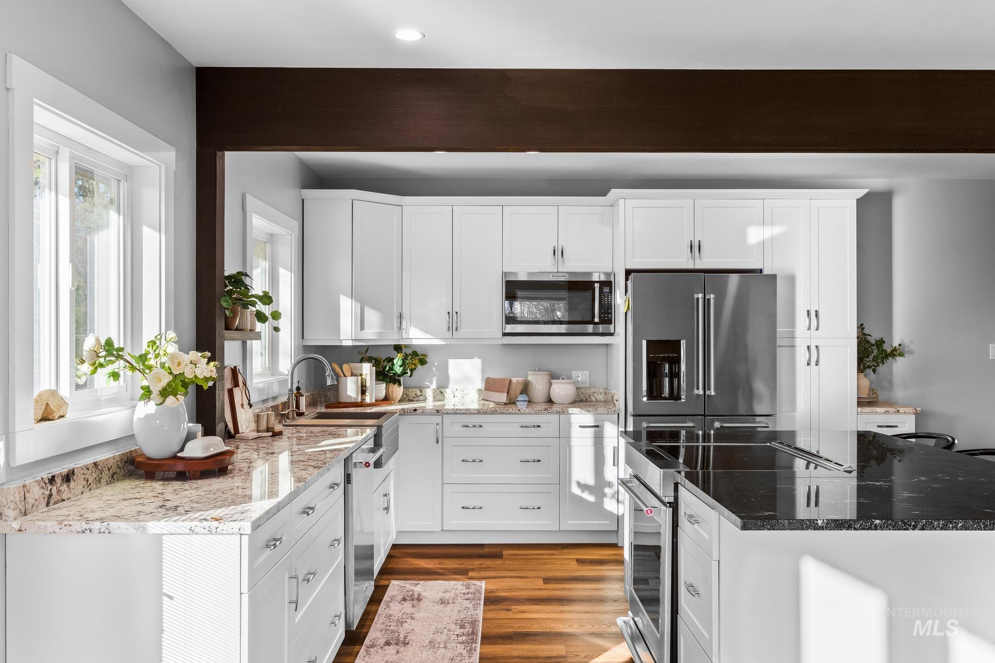 Kitchen featuring white cabinets, dark stone counters, stainless steel appliances, and dark wood finished floors