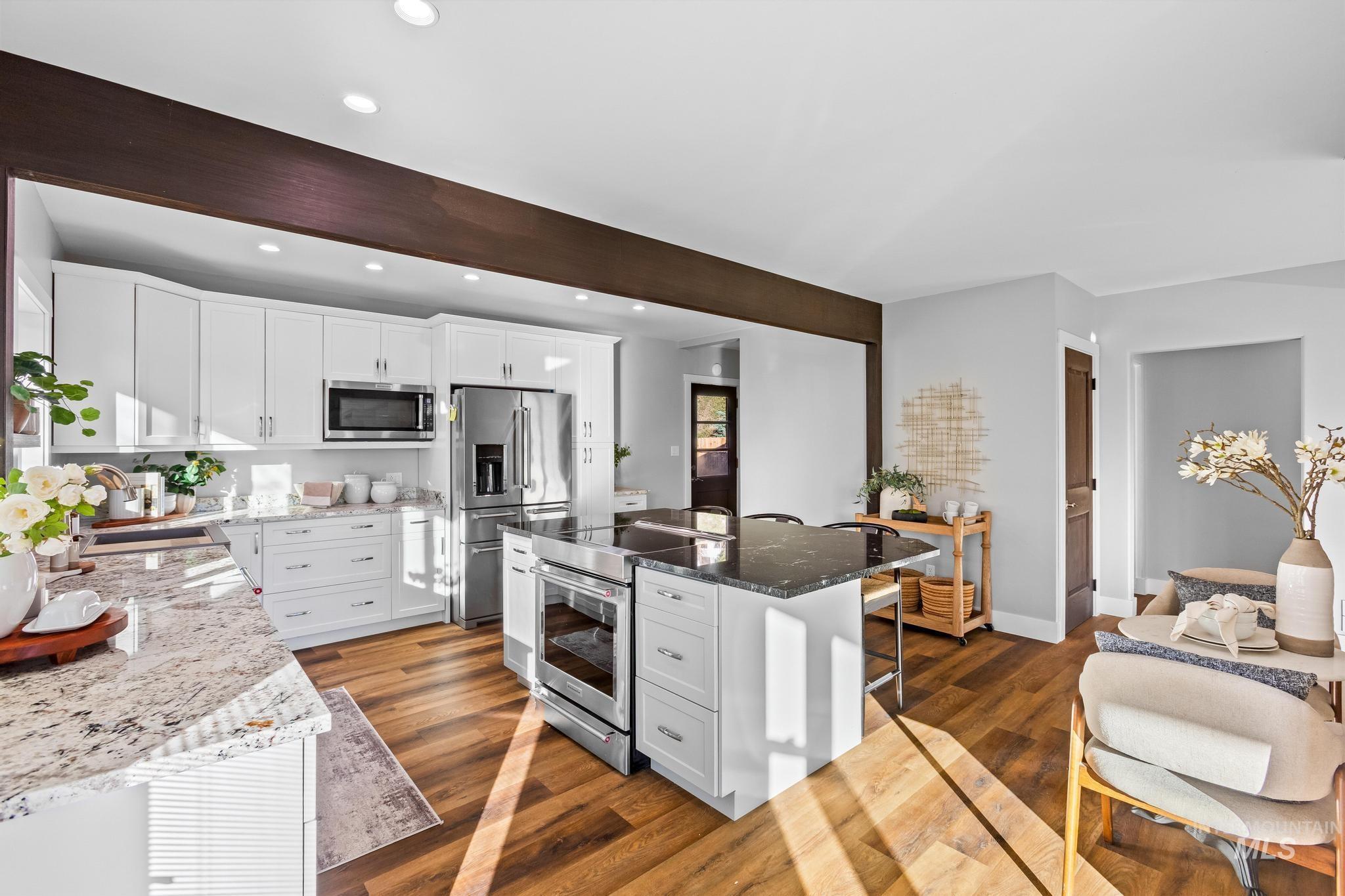Kitchen with white cabinetry, dark stone countertops, appliances with stainless steel finishes, a kitchen bar, and dark wood-type flooring