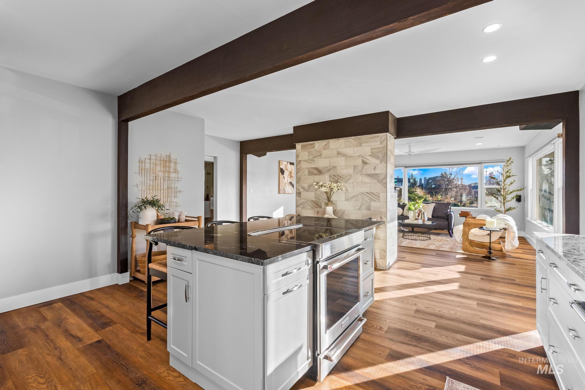 Kitchen featuring a kitchen bar, white cabinetry, dark stone counters, stainless steel electric stove, and beamed ceiling