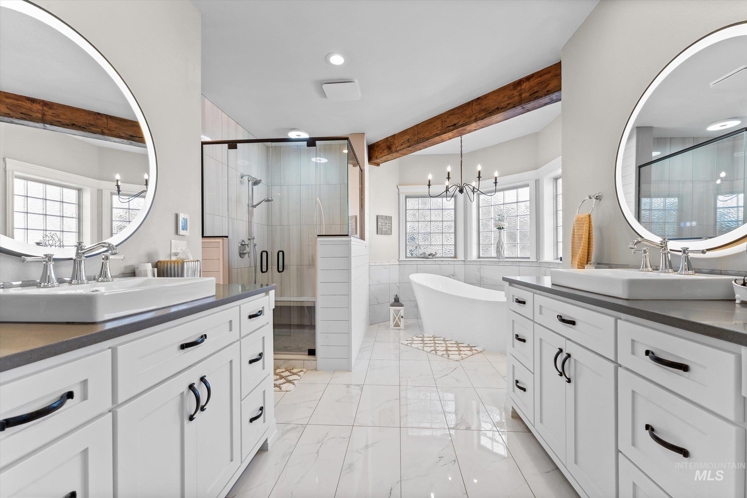 Bathroom featuring beamed ceiling, tile walls, a freestanding bath, two vanities, and a shower stall