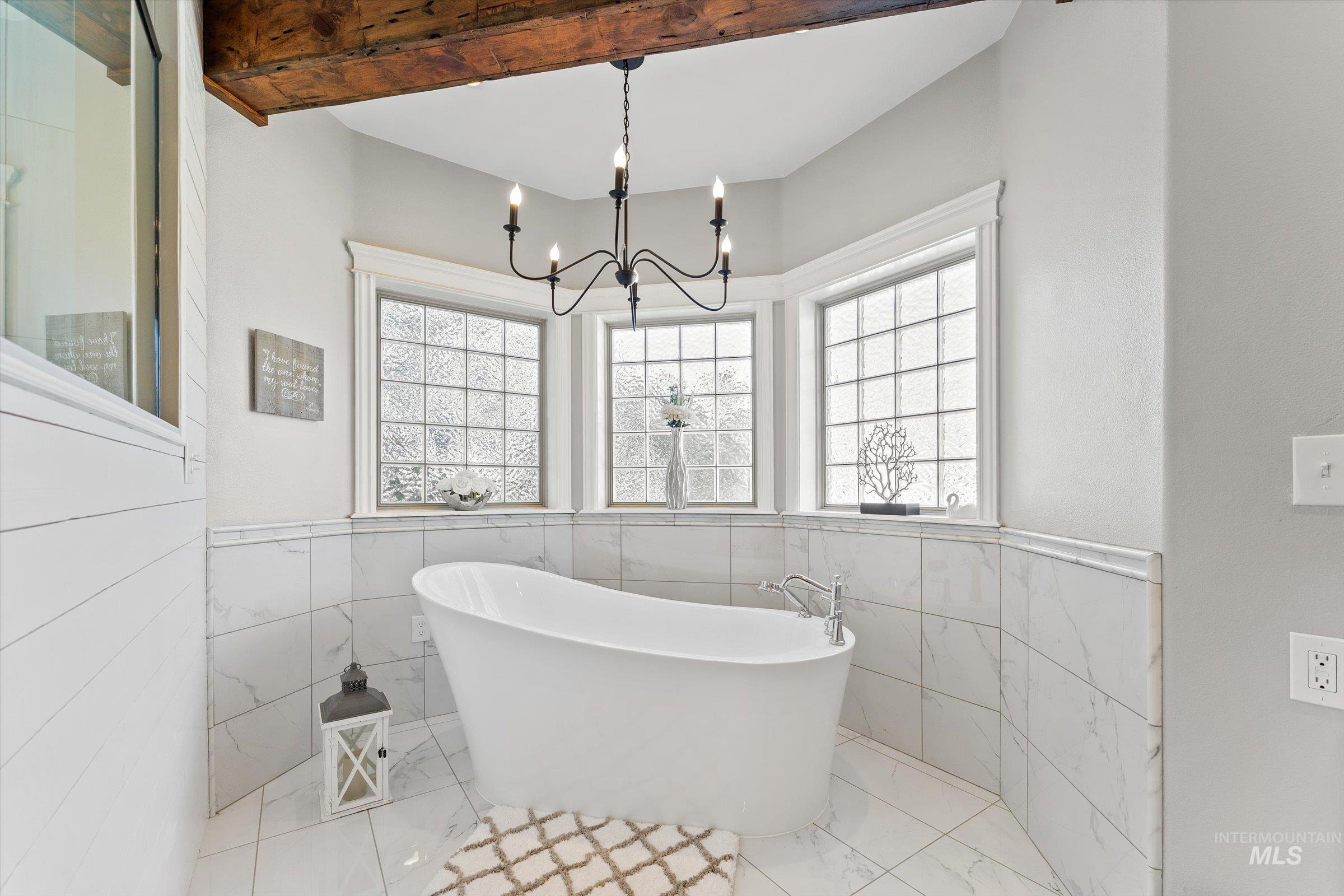 Bathroom featuring a freestanding bath, tile walls, plenty of natural light, wainscoting, and beam ceiling